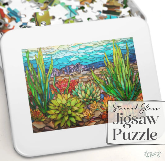A gift-ready puzzle tin with vibrant stained glass artwork of desert succulents and mountains is labeled Stained Glass Succulents Jigsaw Puzzle. Perfect for enthusiasts, it offers hours of artistic enjoyment.