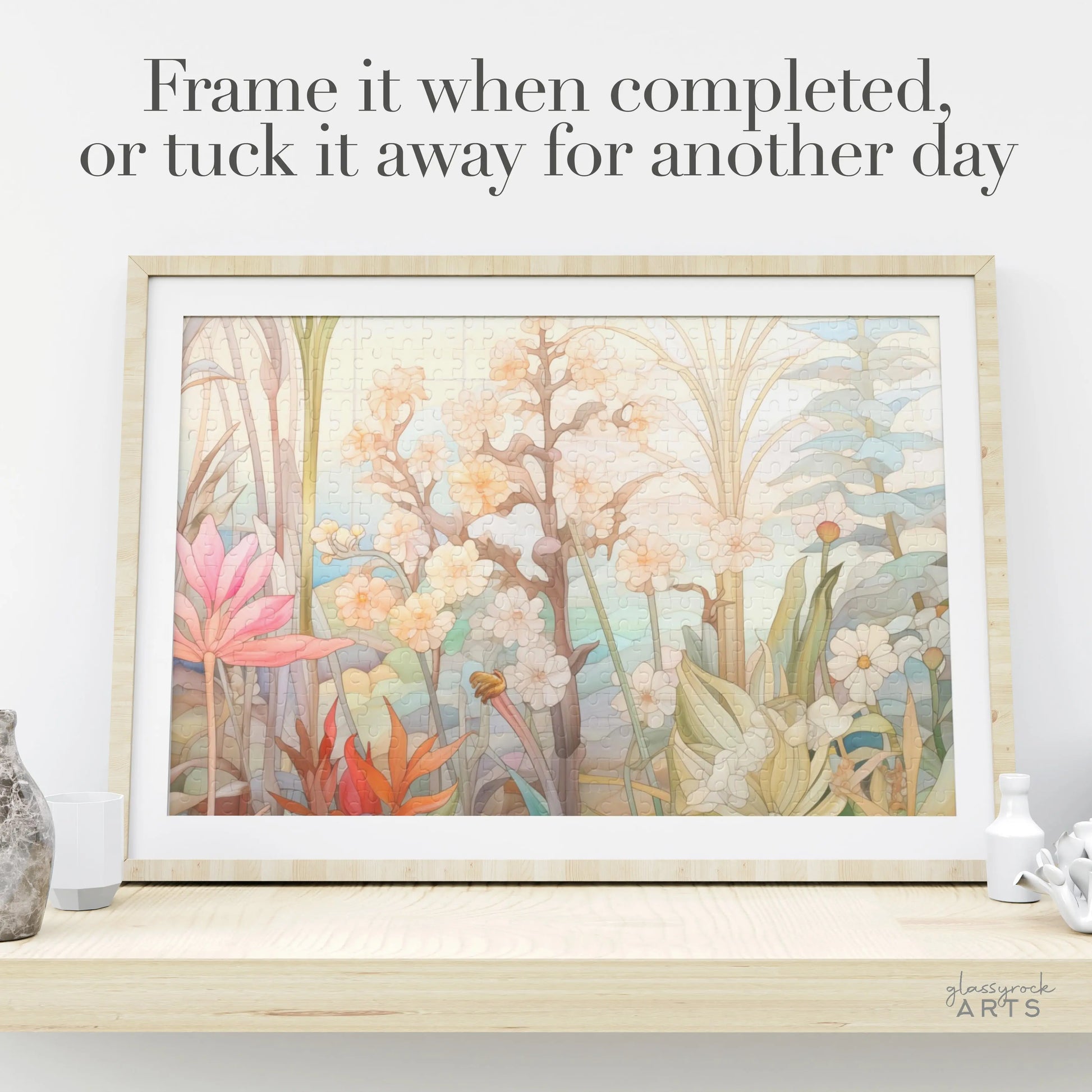 The Summer Botanicals Jigsaw Puzzle, with a soft pastel floral design, is framed on a wooden shelf. Ideal for puzzle enthusiasts, it reads Frame it when completed, or tuck it away for another day. A small plant and decorative item accompany the display.