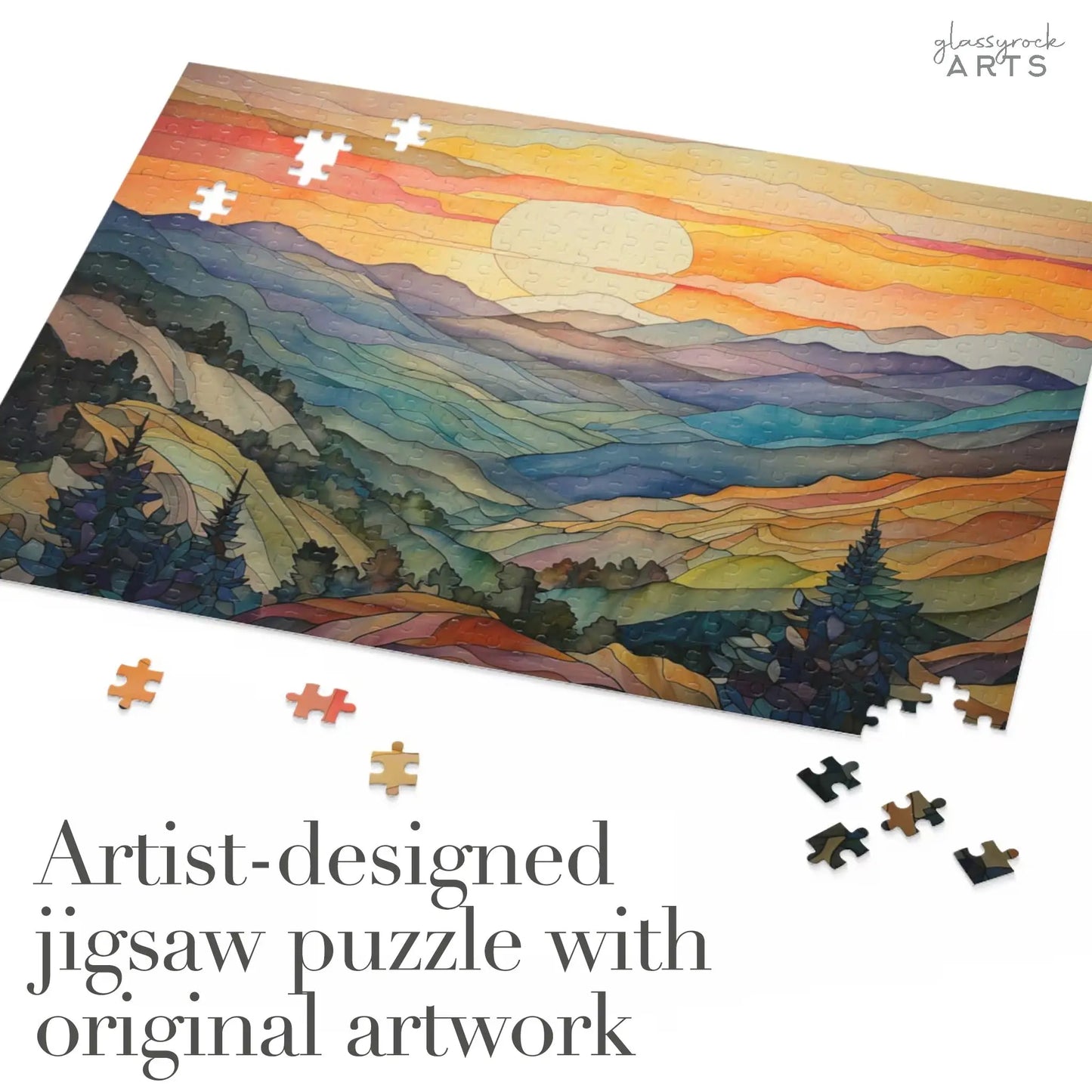 The Sunset Mountains Jigsaw Puzzle features a vibrant, stylized landscape of mountains and a setting sun. Scattered pieces surround the partially completed puzzle. Text reads, Artist-designed jigsaw puzzle with original artwork—an ideal stained glass gift for nature lovers.