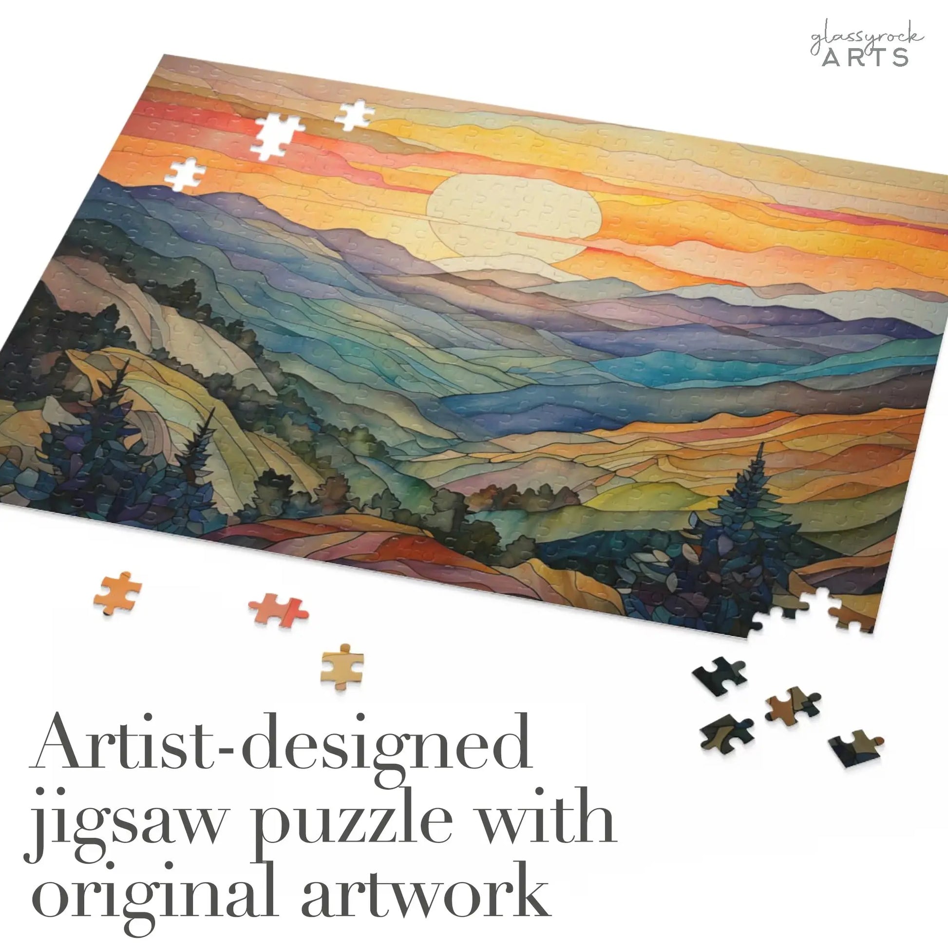 The Sunset Mountains Jigsaw Puzzle features a vibrant, stylized landscape of mountains and a setting sun. Scattered pieces surround the partially completed puzzle. Text reads, Artist-designed jigsaw puzzle with original artwork—an ideal stained glass gift for nature lovers.