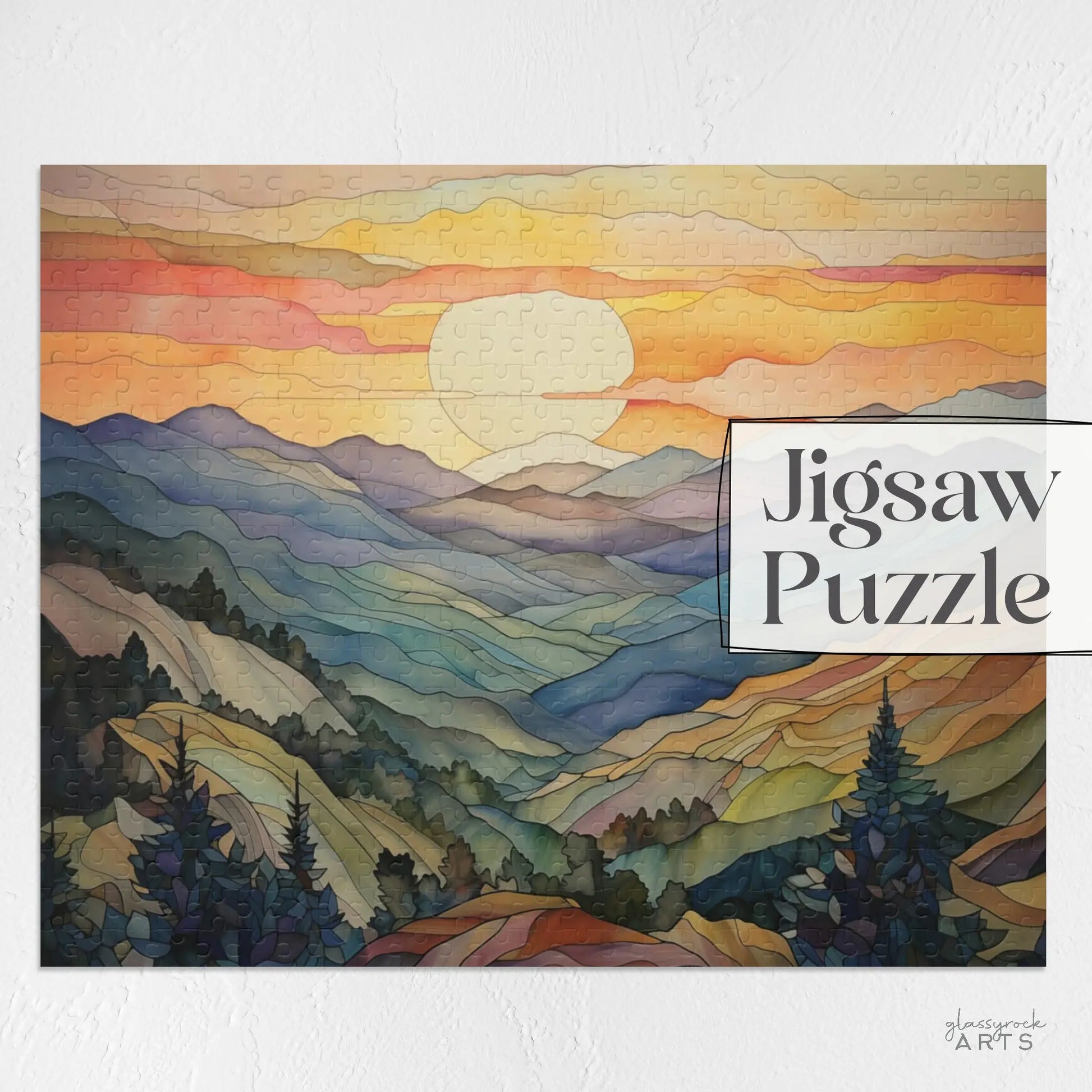 The Sunset Mountains Jigsaw Puzzle displays a vibrant landscape at dusk with orange, pink, and yellow skies over dark green pines. The Jigsaw Puzzle text appears on the right. Ideal for nature enthusiasts.