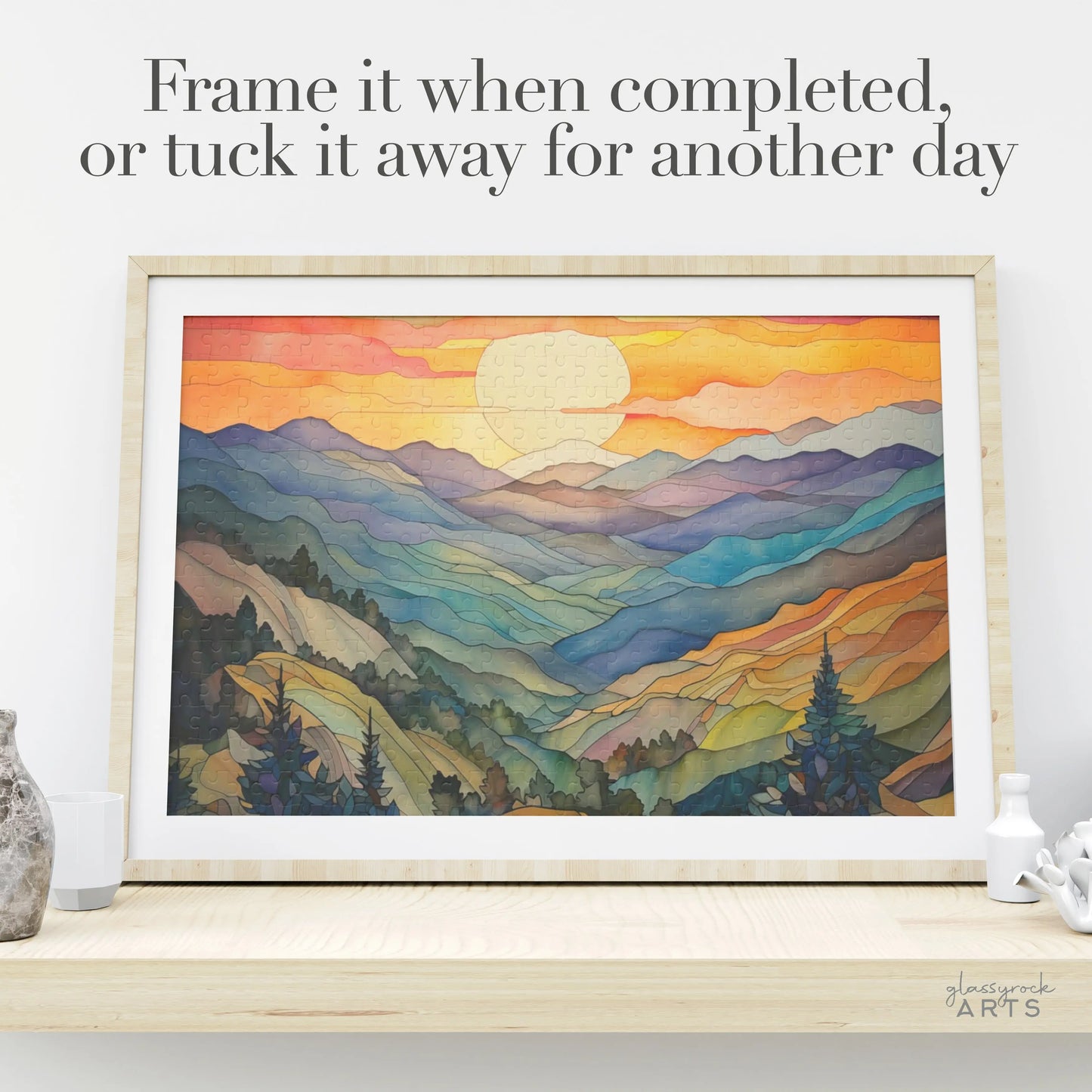 The Sunset Mountains Jigsaw Puzzle features a vivid landscape, framed on a shelf with the words, Frame it when completed, or tuck it away for another day. Its ideal for nature lovers and pairs perfectly with stained glass gifts showcased nearby.