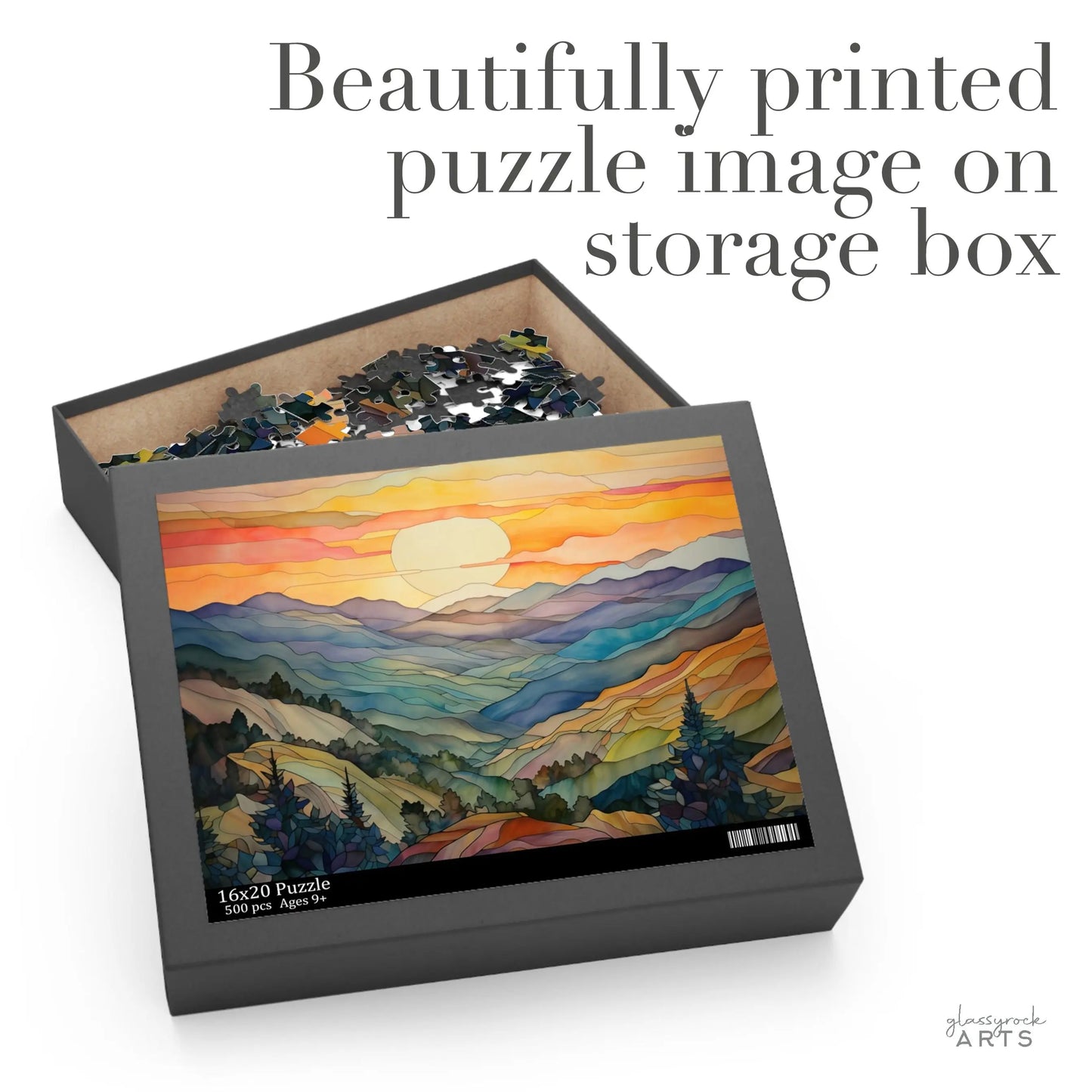 An open puzzle box with scattered pieces reveals a vivid sunset mountains image on the lid. Text reads, Beautifully printed puzzle image on storage box, making the Sunset Mountains Jigsaw Puzzle a perfect gift for any nature lover.
