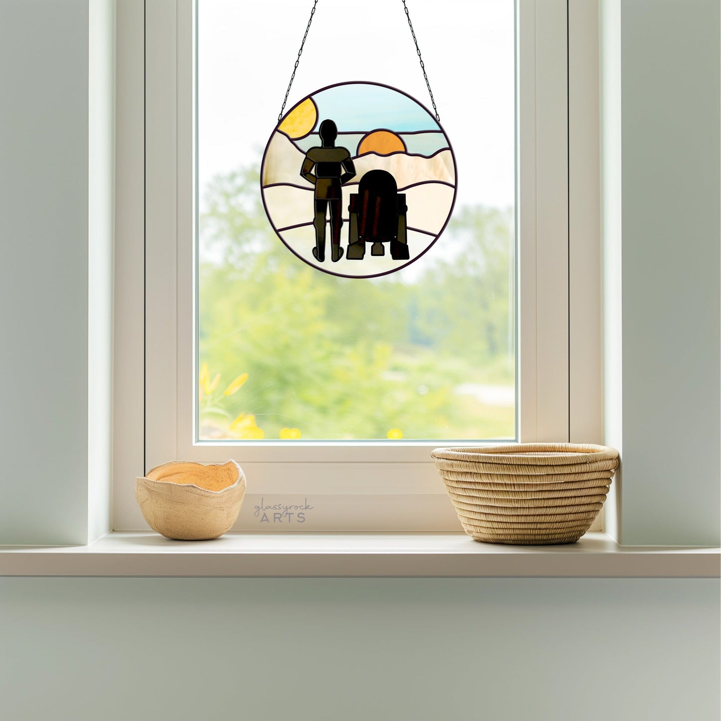 A Tatooine Landscape Stained Glass Pattern hangs in the window, showcasing two figures against a scenic backdrop with cascading light. Below, two woven baskets sit on the windowsill.