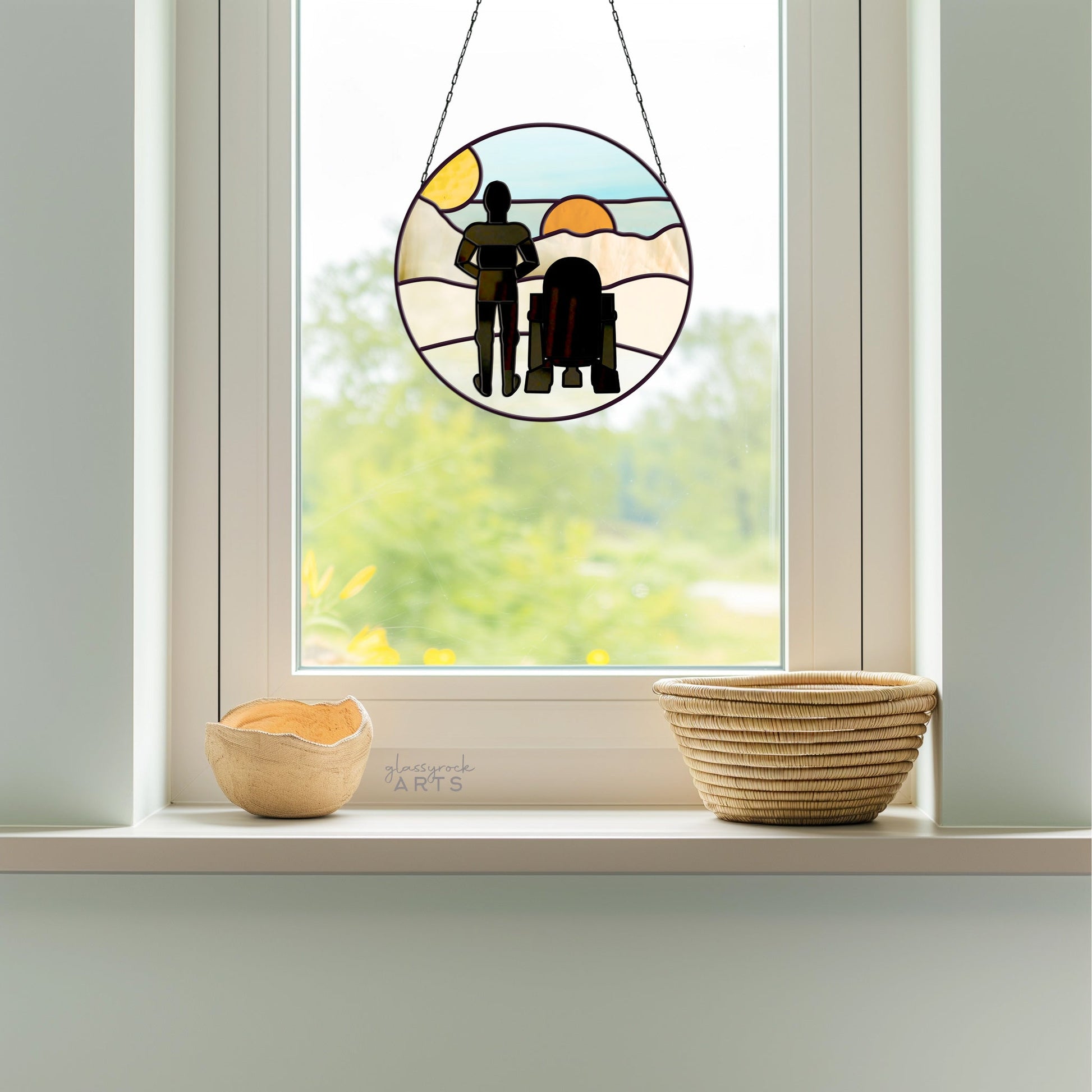 A Tatooine Landscape Stained Glass Pattern hangs in the window, showcasing two figures against a scenic backdrop with cascading light. Below, two woven baskets sit on the windowsill.