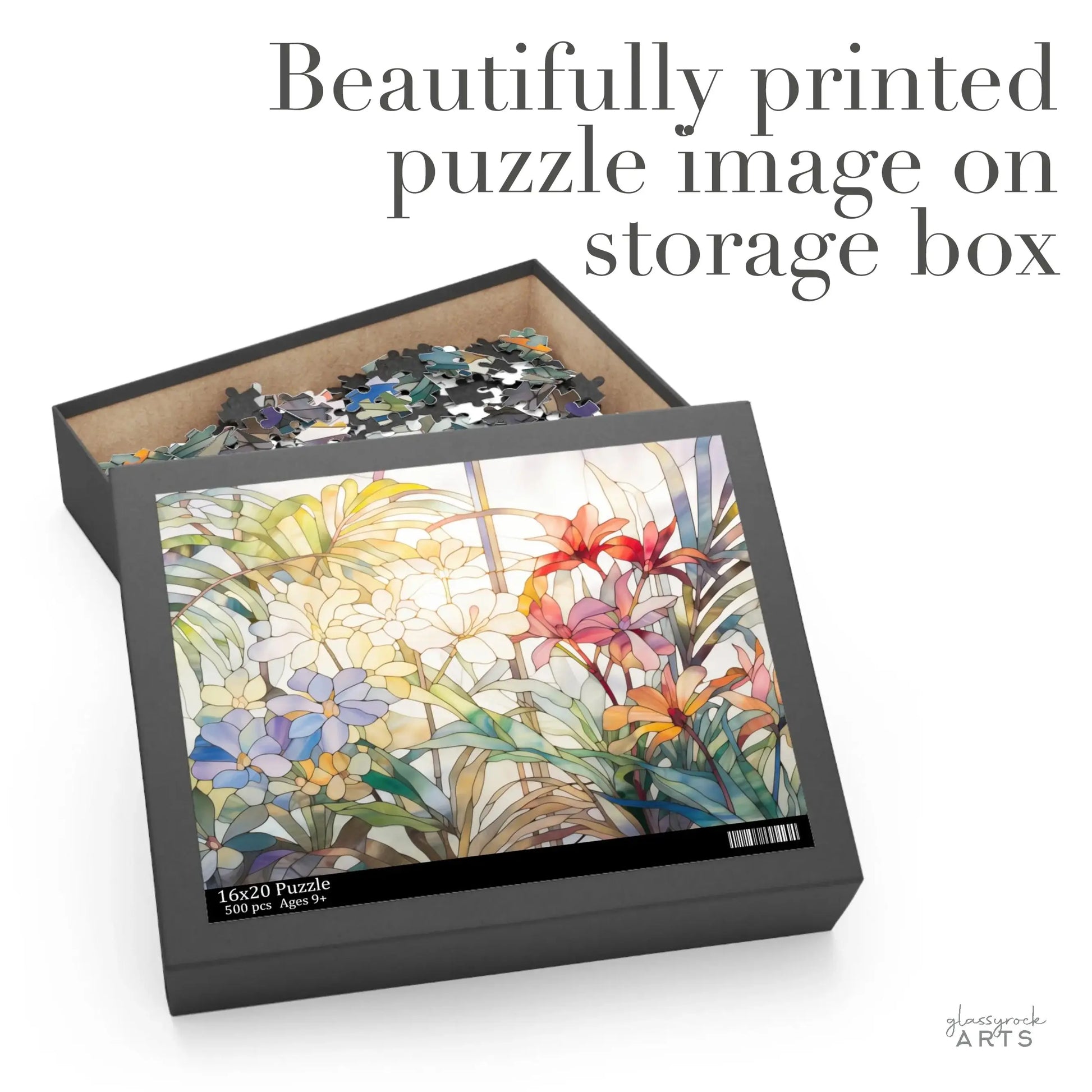 The Tropical Blooms Jigsaw Puzzle features a vibrant floral design with tropical flowers like lilies and lush leaves on its lid. Open the box to reveal mixed puzzle pieces inside. The text reads: Beautifully printed puzzle image on storage box—a perfect art gift.