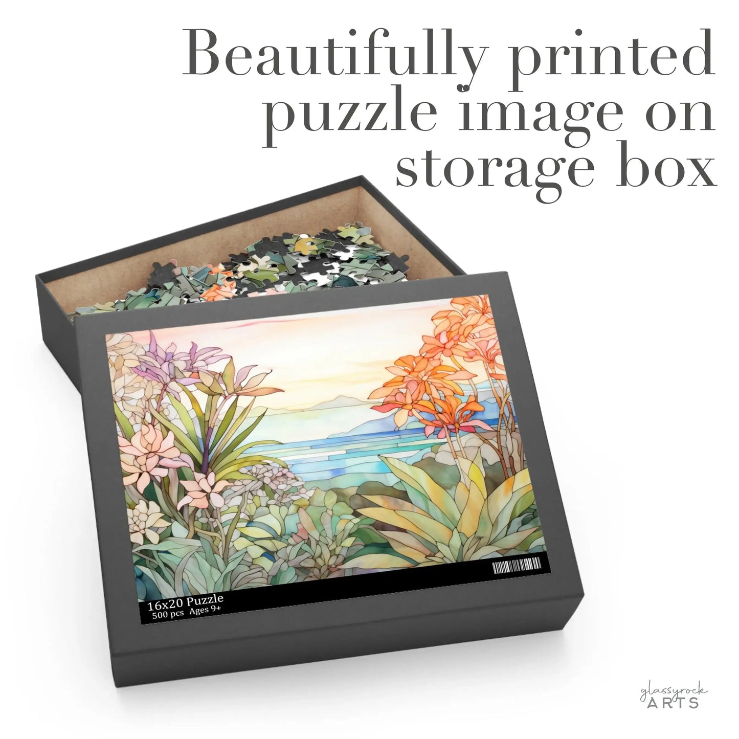 The open Tropical Botanicals Jigsaw Puzzle box showcases a serene landscape and vibrant tropical botanicals, with a stained glass-inspired design. Text above reads, Beautifully printed puzzle image on storage box.