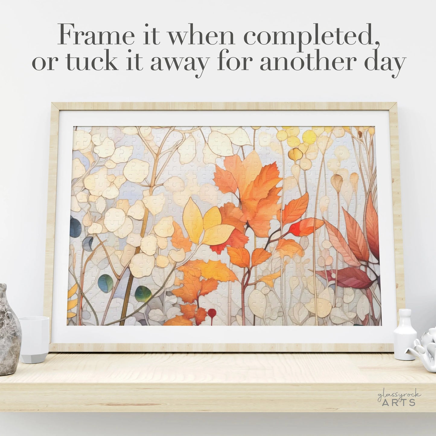 A framed puzzle titled Winter Botanicals Jigsaw Puzzle rests on a wooden surface, showcasing vibrant stained glass-inspired leaves and branches. Accompanying text suggests, Frame it when completed, or tuck it away for another day, capturing the essence of falls beauty.