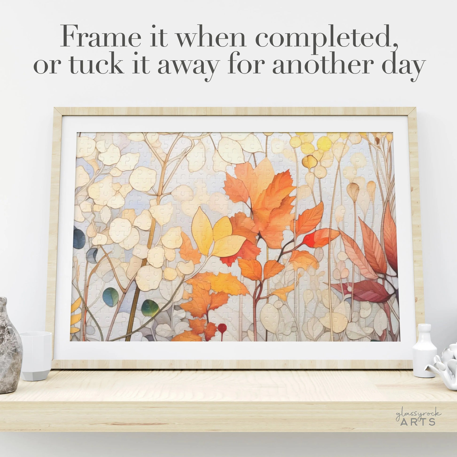 A framed puzzle titled Winter Botanicals Jigsaw Puzzle rests on a wooden surface, showcasing vibrant stained glass-inspired leaves and branches. Accompanying text suggests, Frame it when completed, or tuck it away for another day, capturing the essence of falls beauty.