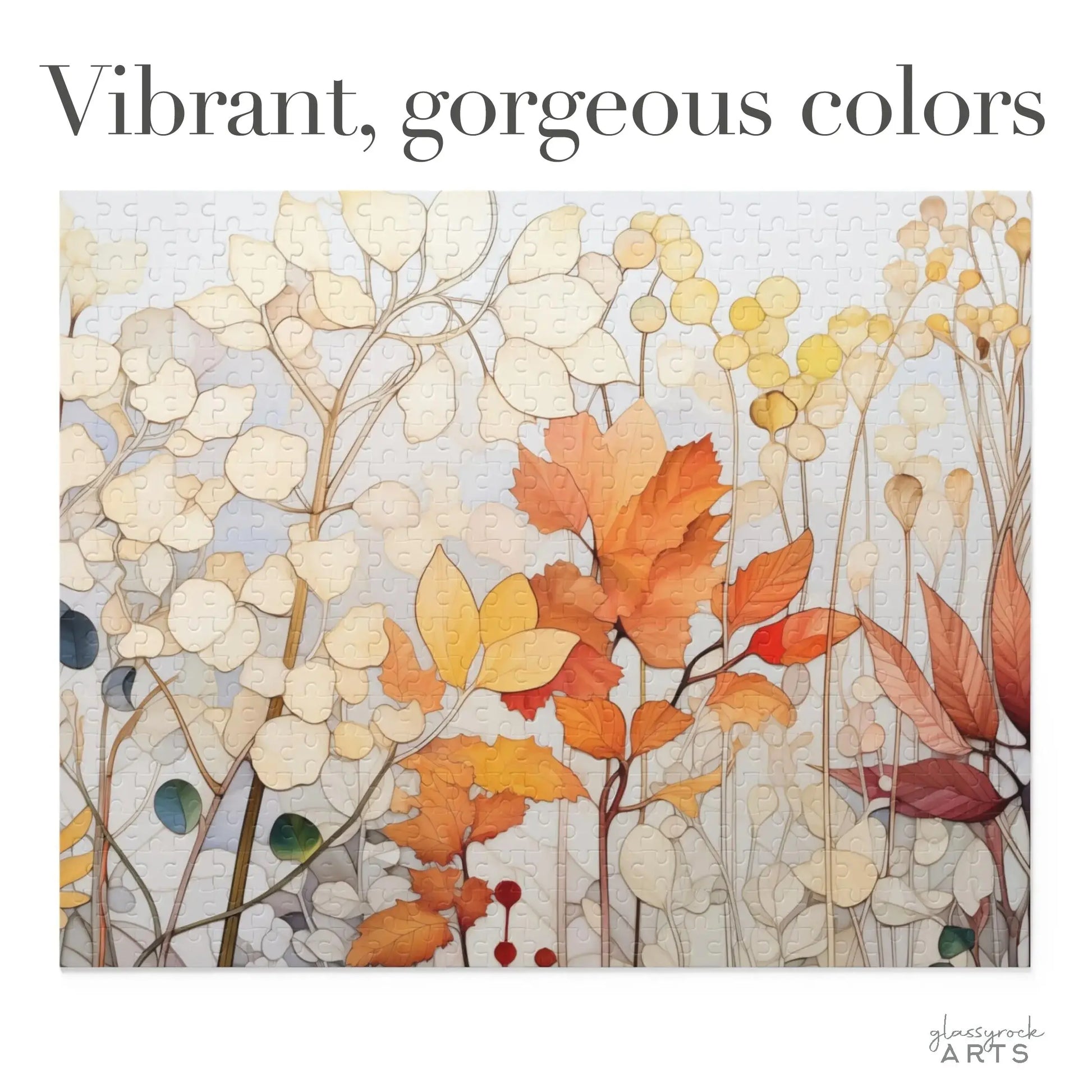 The Winter Botanicals Jigsaw Puzzle showcases autumn leaves and branches in stained glass-inspired reds, oranges, and yellows. Set against a grayish-white background, the top displays bold text: Vibrant, gorgeous colors.