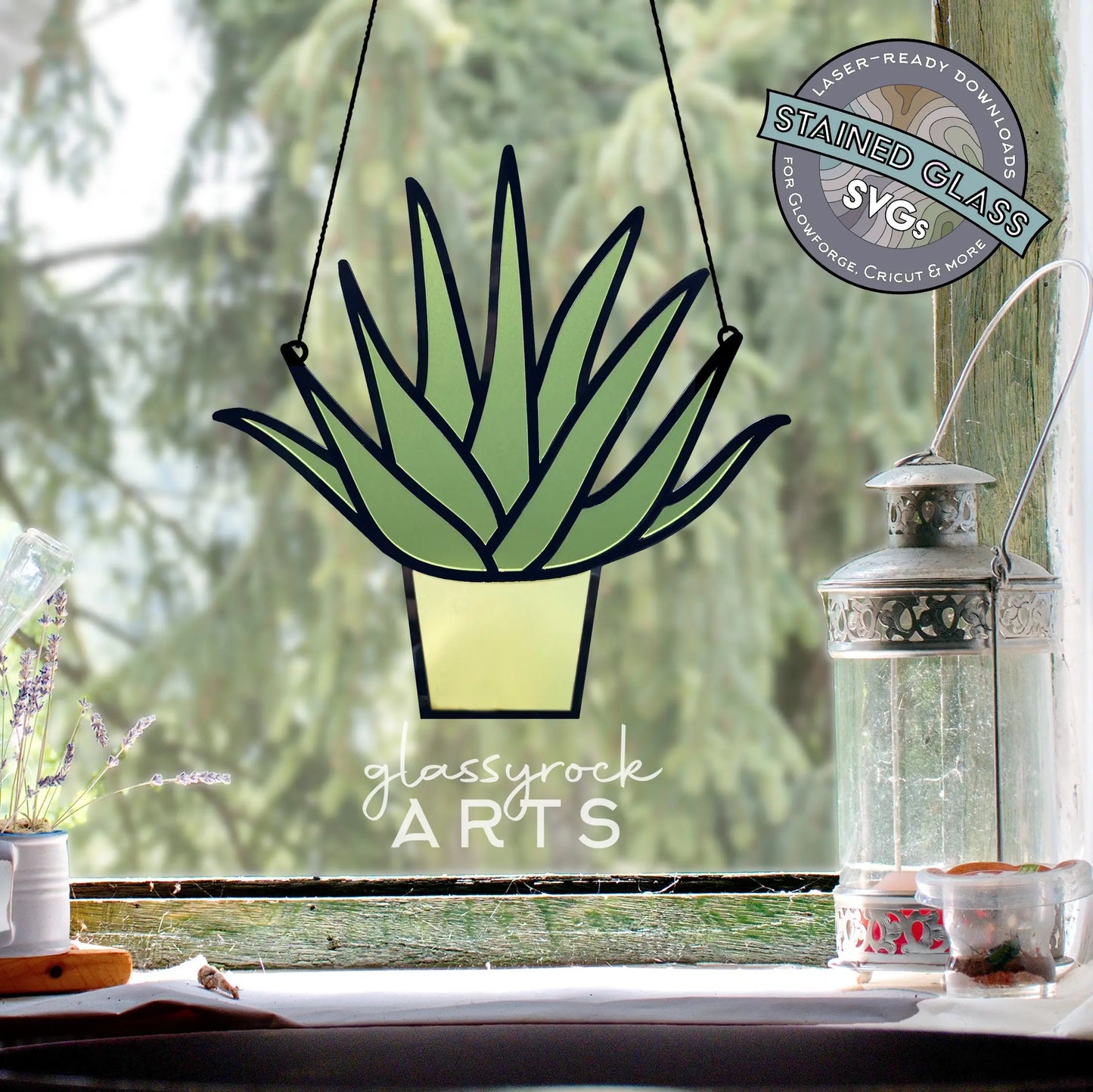 A stained glass aloe plant design hangs by the window, with a metal lantern and small vase on the sill. The logo Glassyrock Arts is beneath it, accompanied by a circular label that reads Stained Glass Aloe Plant, SVG for Laser Cutting.