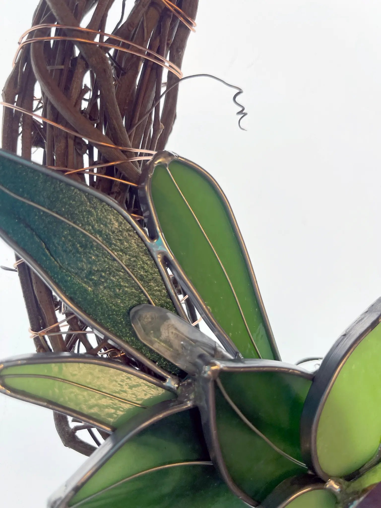 Close-up of the Handmade Botanical Stained Glass Wreath with various green leaves and copper wire accents. Vines twist around, adding texture while a softly blurred background highlights the designs intricacy.