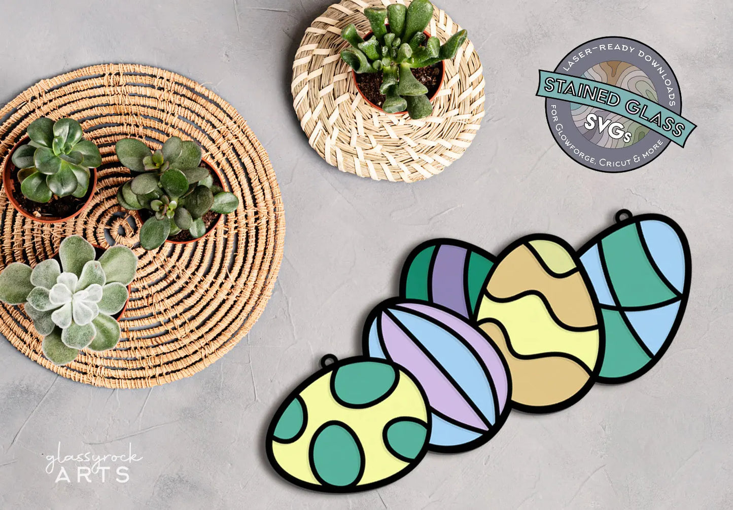 A woven mat showcases small potted succulents next to elegant Easter decorations, including colorful, stained glass-style eggs with various patterns and pastel shades on a gray surface. A badge highlights the Stained Glass Easter Eggs SVGs laser cut file for downloadable designs.