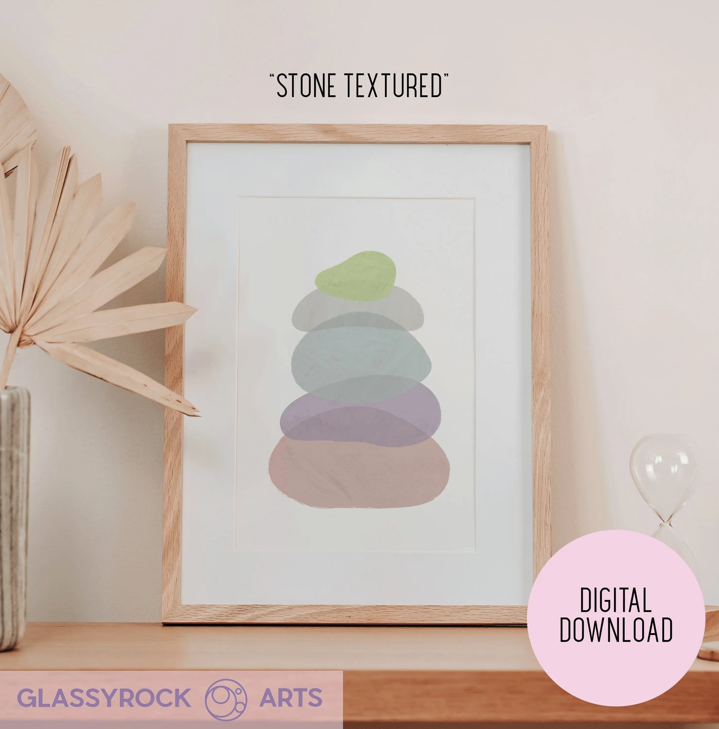 A framed digital download of Pastel Painted Boho Stone Shapes sits on a table, showcasing abstract pastel colors. A dried plant accents the left side, and a tiny hourglass is on the right. Ideal for fans of digital art printables seeking an instant digital file with Stone Textured flair.