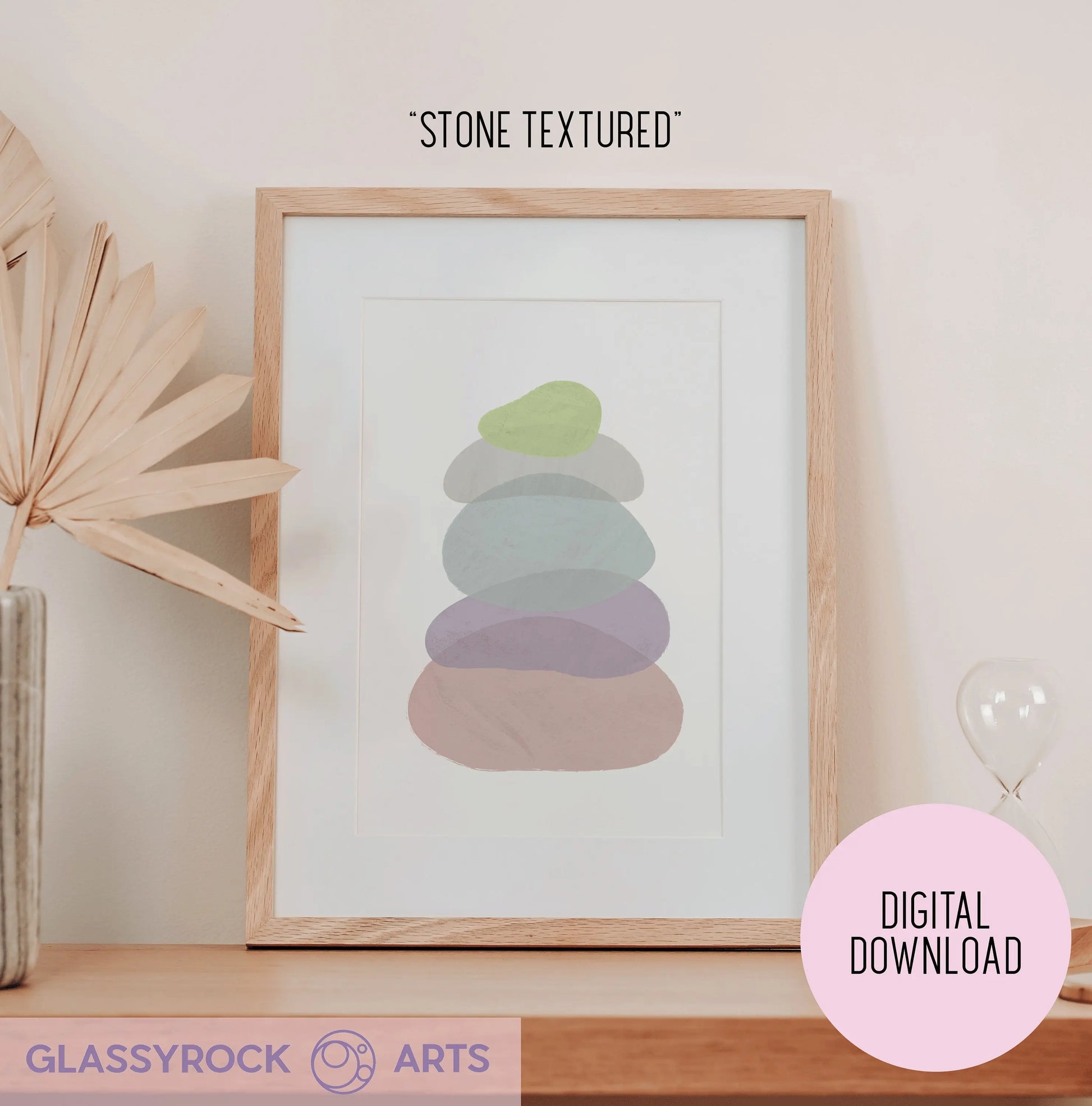A framed digital download of Pastel Painted Boho Stone Shapes sits on a table, showcasing abstract pastel colors. A dried plant accents the left side, and a tiny hourglass is on the right. Ideal for fans of digital art printables seeking an instant digital file with Stone Textured flair.