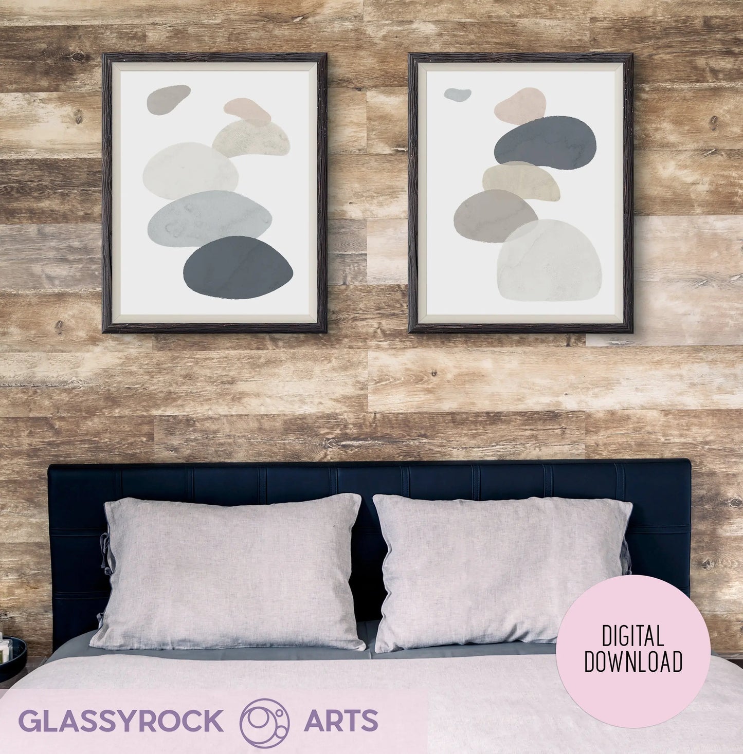 Two Abstract Watercolor Stone Shapes prints from Glassyrock Arts hang above a dark blue headboard and gray-pillowed bed, framed by wooden frames against a rustic wood backdrop; marked as a digital download.