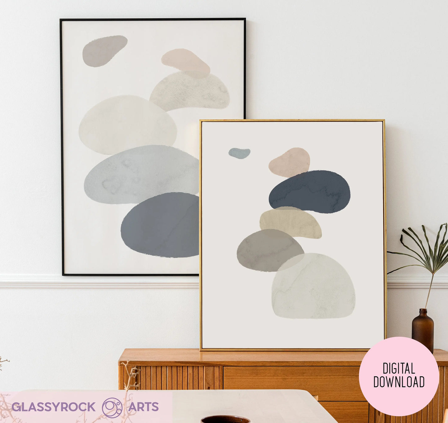 The Abstract Watercolor Stone Shapes Digital Art features two muted-tone prints with overlapping shapes on a wood sideboard, accompanied by a small potted plant. A Digital Download label marks the bottom right corner, emphasizing the instant file experience.