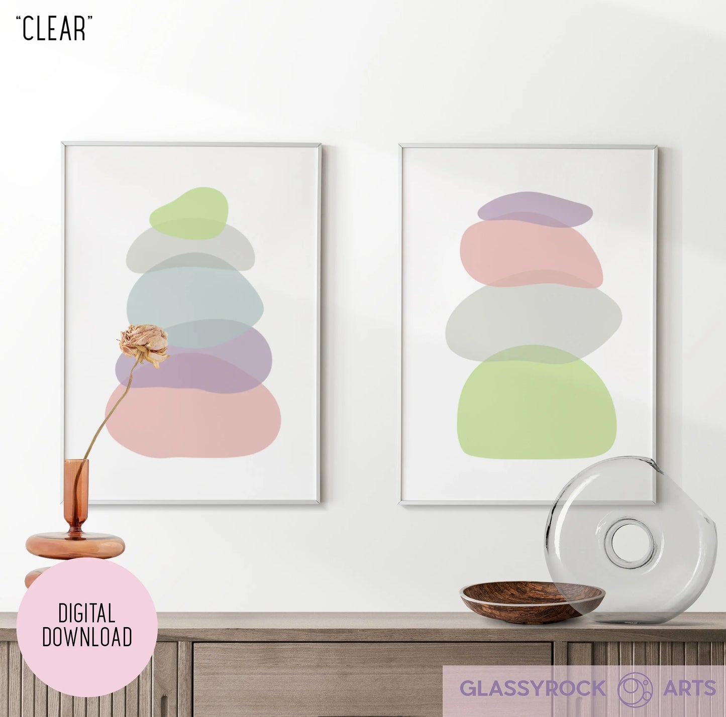 Two abstract pastel prints of modern stone shapes by Glassyrock Arts are displayed on the wall. Below, a wooden surface holds a glass vase with one dried flower, boho accents like a round glass piece, and a wooden bowl. Available as digital downloads titled Pastel Clear Modern Stone Shapes.