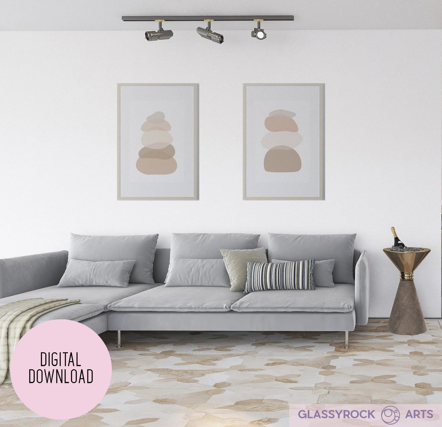 A modern living room boasts a gray sectional sofa, patterned cushions, and a small table with a sculpture. Two minimalist Ombre Nude Stone Shapes Digital Artwork prints adorn the wall. The floor flaunts a beige and white geometric pattern, while track lighting on the ceiling enhances the serene ambiance.