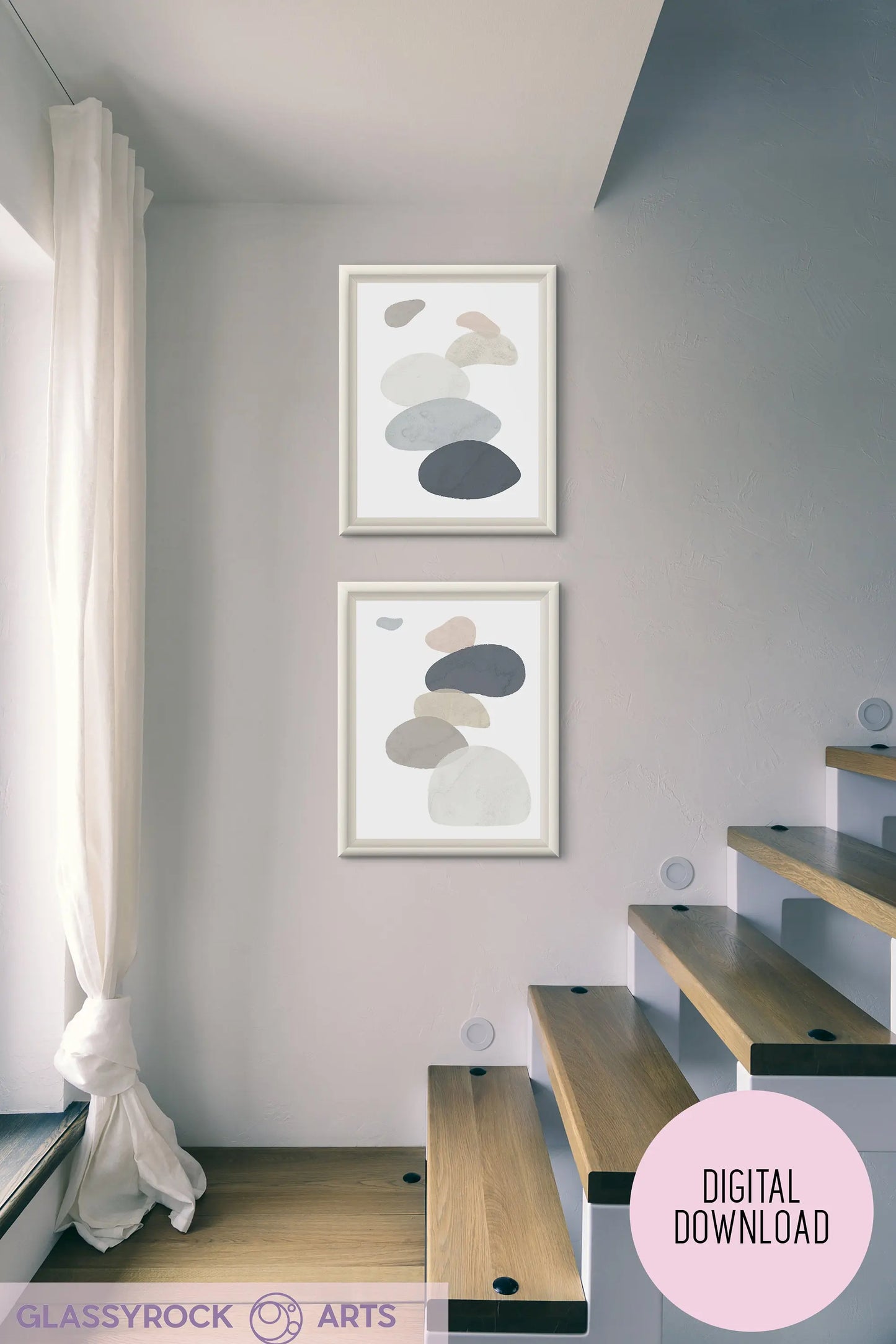 Minimalist interior showcasing two framed abstract paintings with oval shapes similar to Abstract Watercolor Stone Shapes Digital Art in neutral tones adorns a light wall. A wooden staircase with black accents ascends, while sunlight streams through sheer white curtains on the left. Instant Digital File text appears on the image.