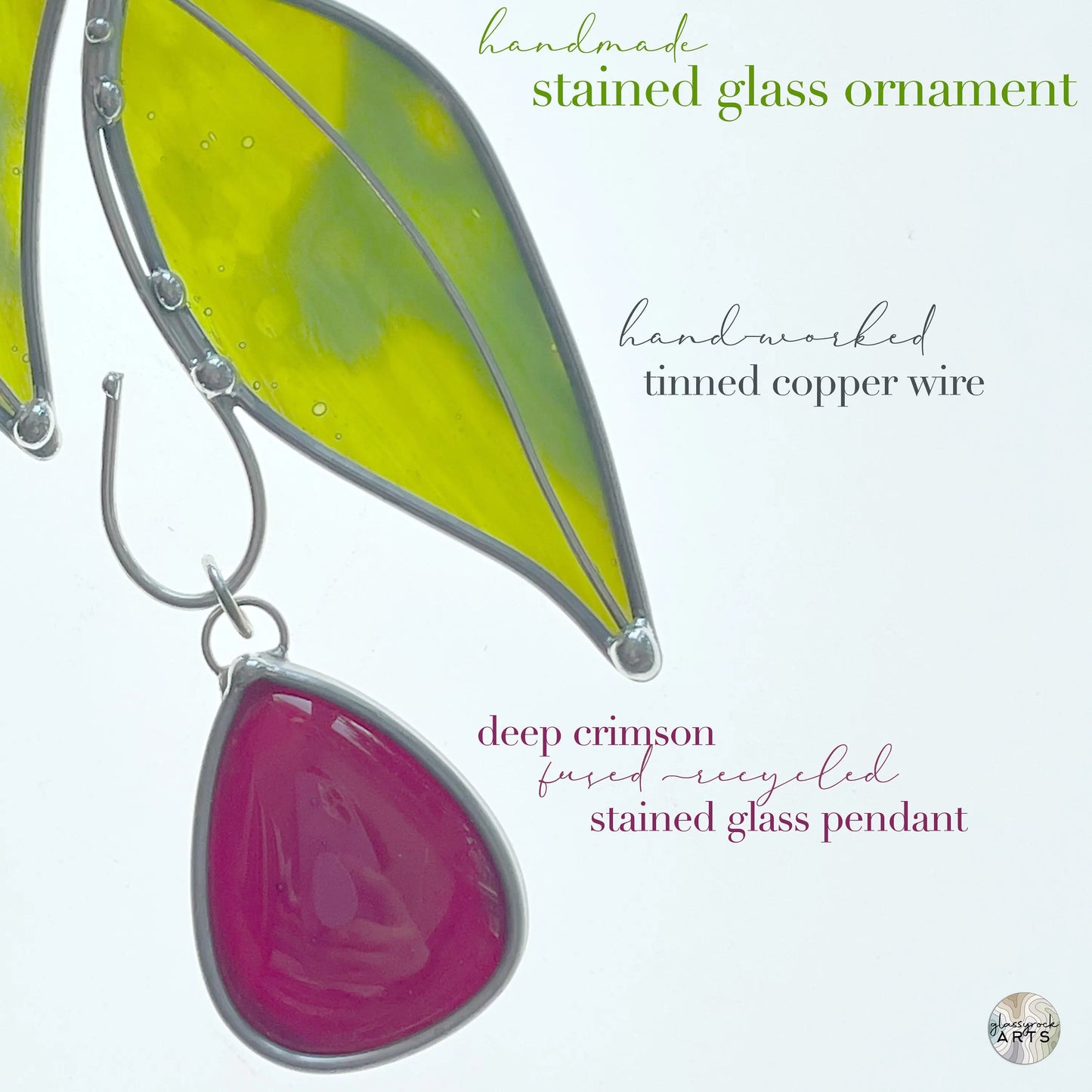 The Handmade Stained Glass Leaf Suncatchers feature green leaves, a deep crimson recycled glass pendant, and handworked tinned copper wire. Decorative text overlays add a unique touch, making it a distinctive ornament for any space.