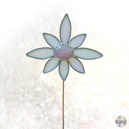 The Handmade Stained Glass Flower Plant Stake with Rose Quartz features seven white petals and a central pink piece, all edged in silver on a thin rod, resembling a delicate plant stake against a soft, blurred white background.