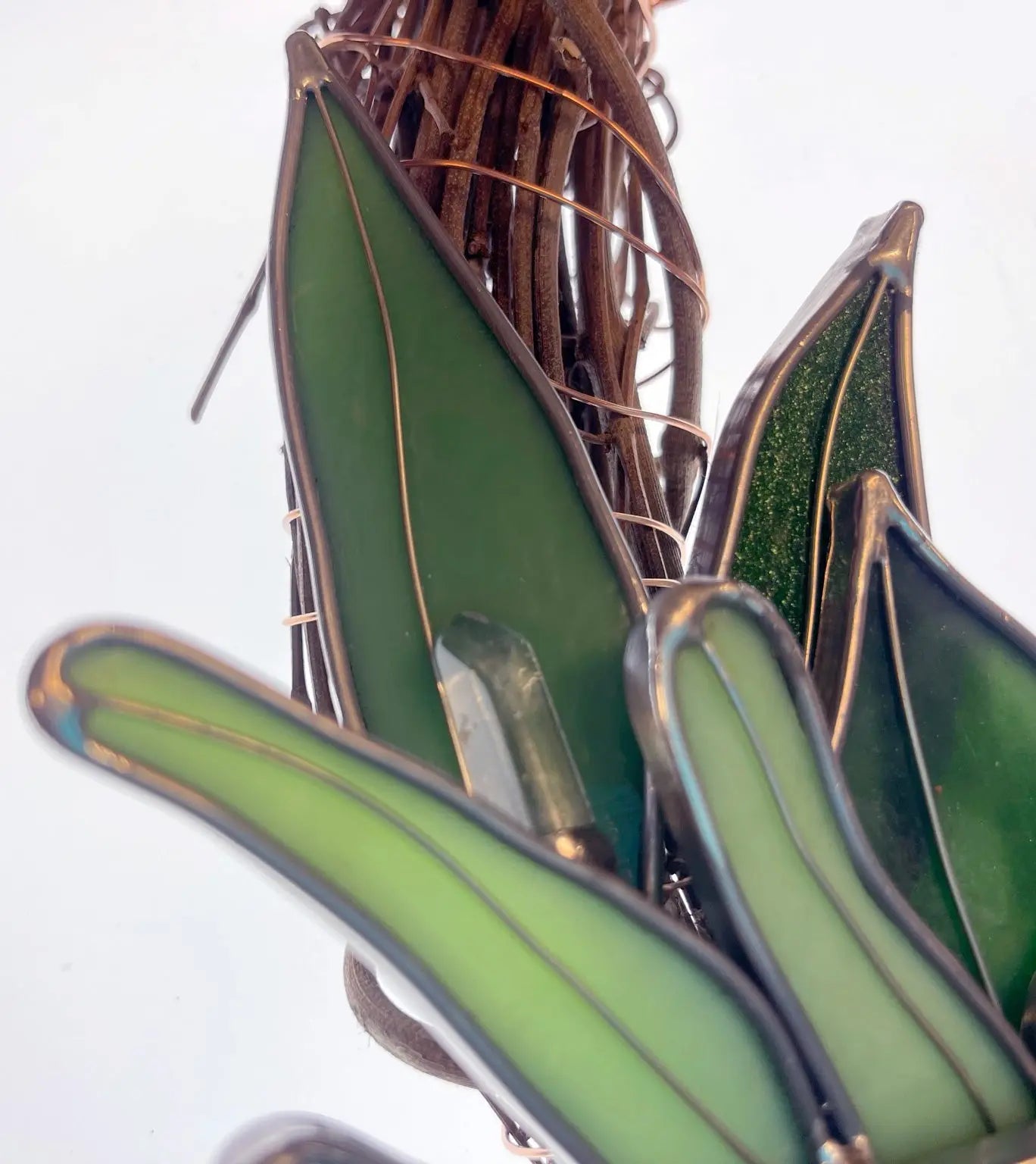Close-up of the Handmade Botanical Stained Glass Wreath, showcasing green leaf-shaped glass, interwoven with thin wire and natural twigs that form a three-dimensional, organic design.