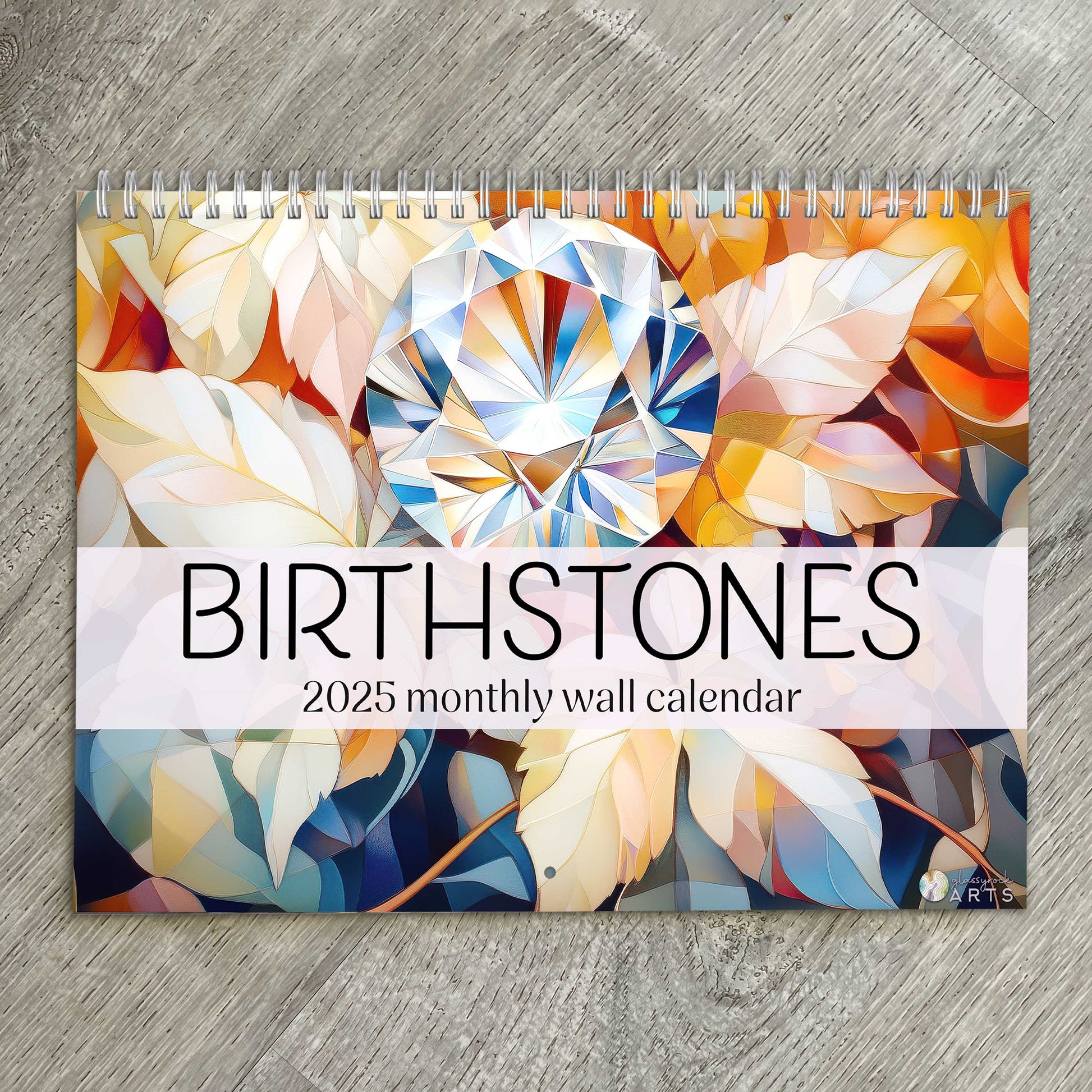 The birthstones calendar, a 2025 monthly wall calendar with gem-themed original artwork, on a wood table surface. 