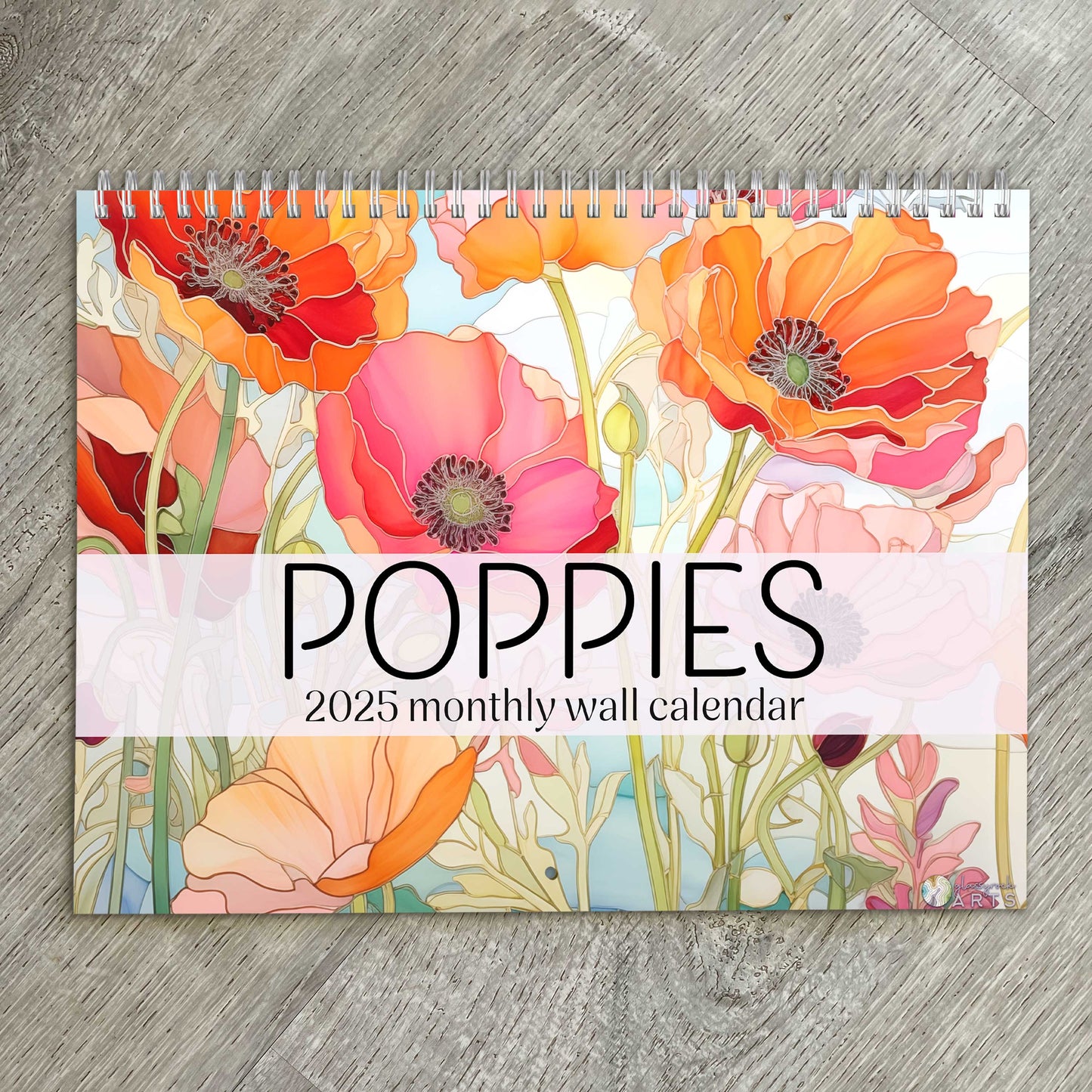 The poppies calendar, a 2025 monthly wall calendar with poppy-themed original artwork, on a wood table surface. 