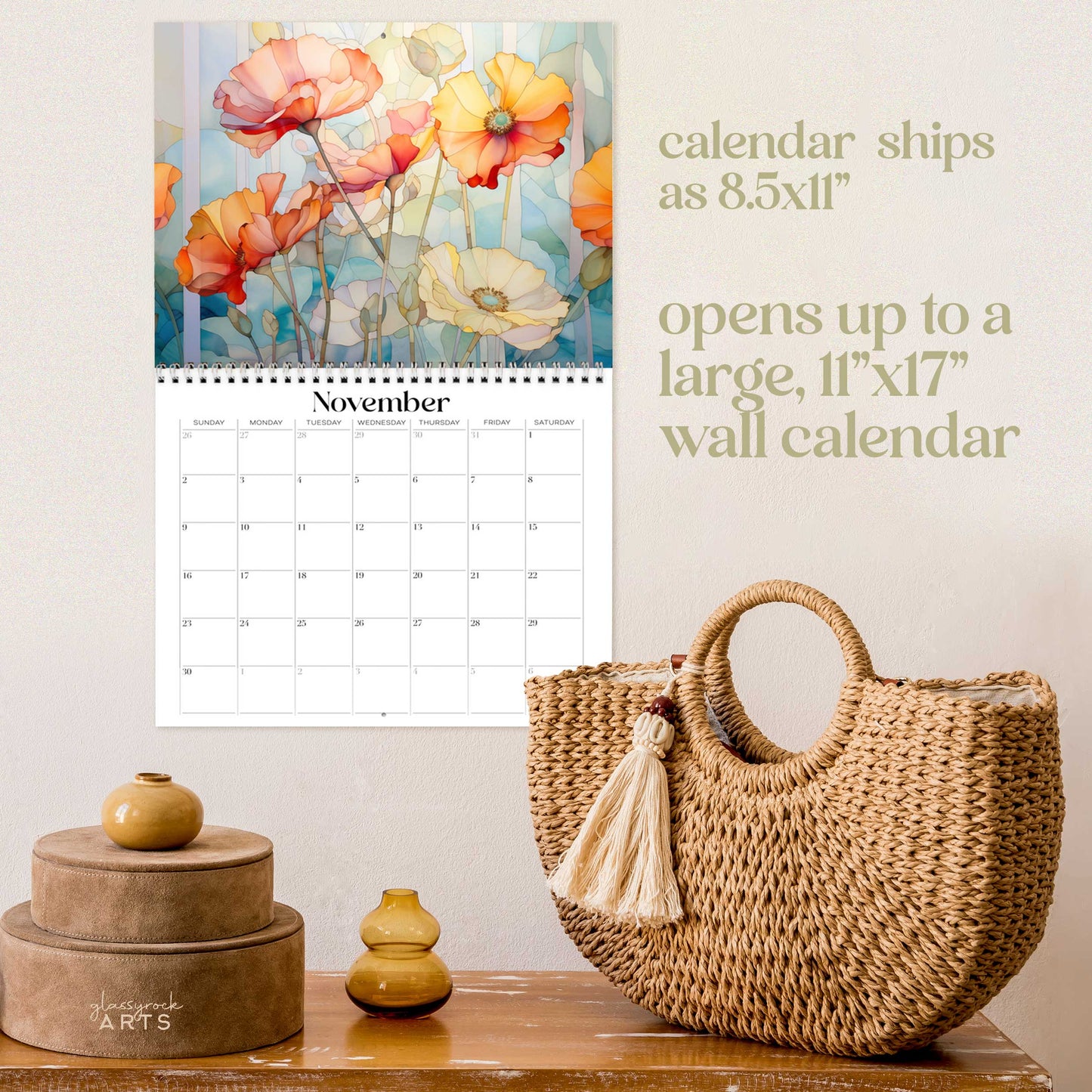 The poppies calendar, a 2025 monthly wall calendar with poppy-themed original artwork, on a wall above a wood table with a wicker purse. The calendar is open to November, showing colorful poppies.