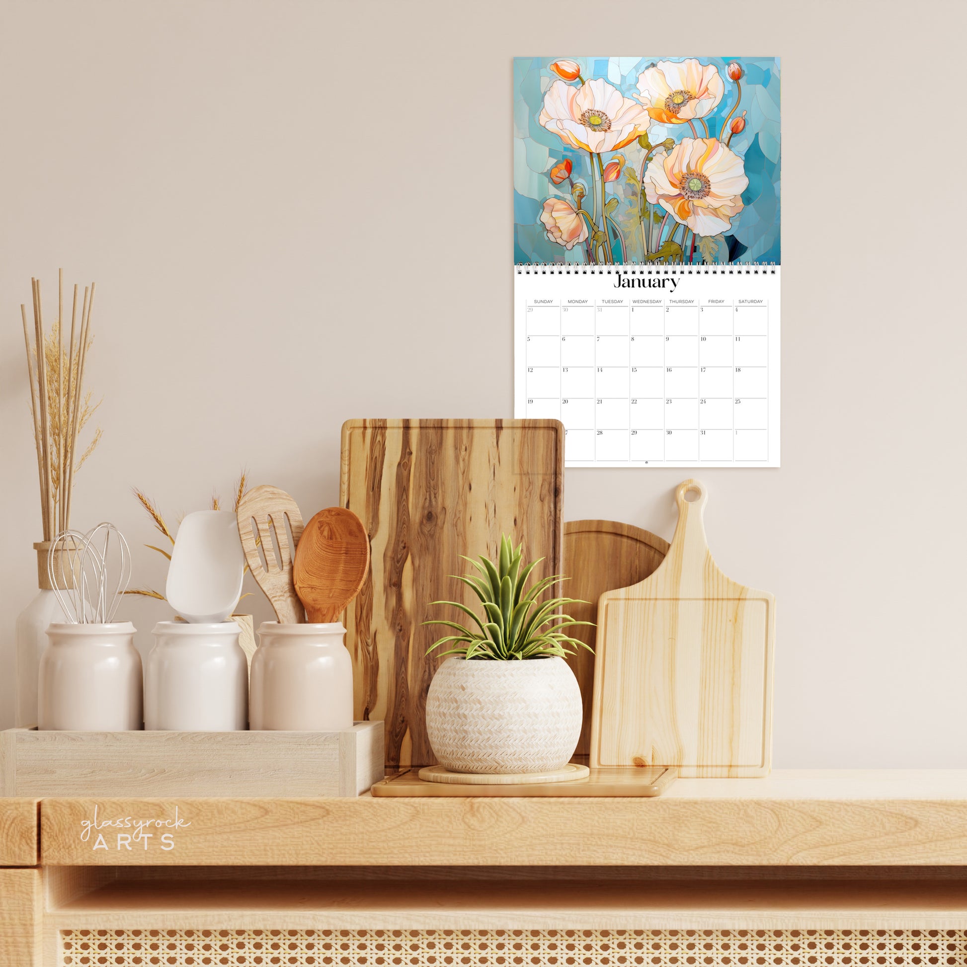 The poppies calendar hanging in a kitchen with kitchen tools below on a counter. 