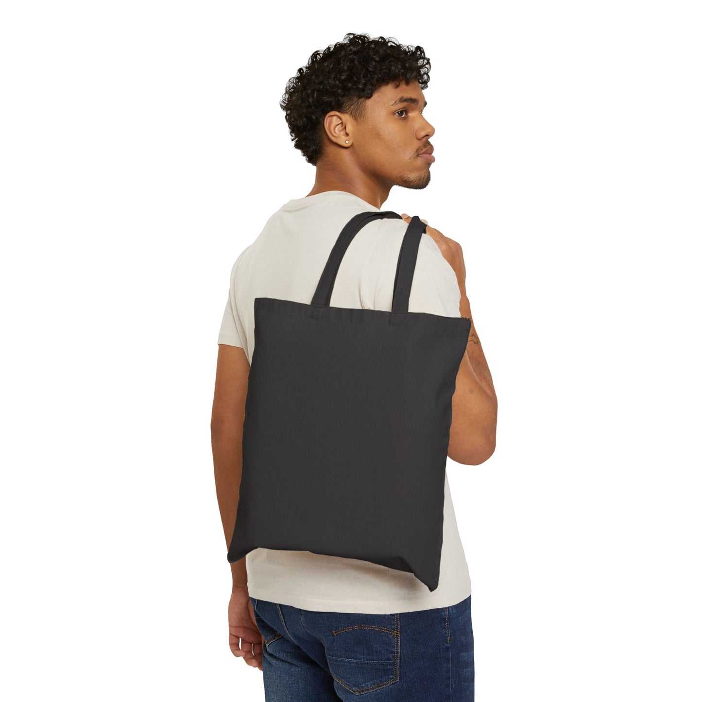 A person with short, curly hair, in a white shirt and jeans, faces left and carries the Stained Glass Sunflower Cotton Canvas Tote Bag over their shoulder against a white background.