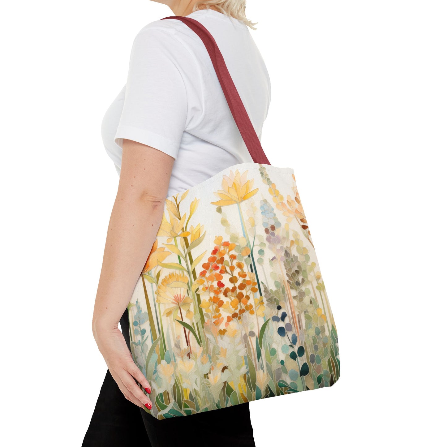 A person wearing a white shirt is holding the Stained Glass Fall Flowers Tote Bag, featuring an original artists design with colorful yellow, orange, and green flowers. The tote has red shoulder straps and is made from durable polyester.