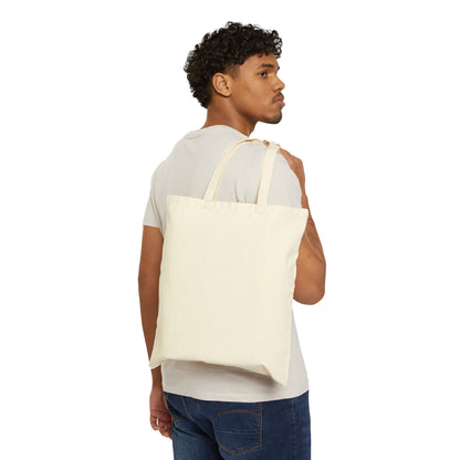 A person with curly hair wearing a white t-shirt and jeans is holding the Stained Glass Heart Cotton Canvas Tote Bag featuring a heart stained glass design in a circular pattern over their shoulder.