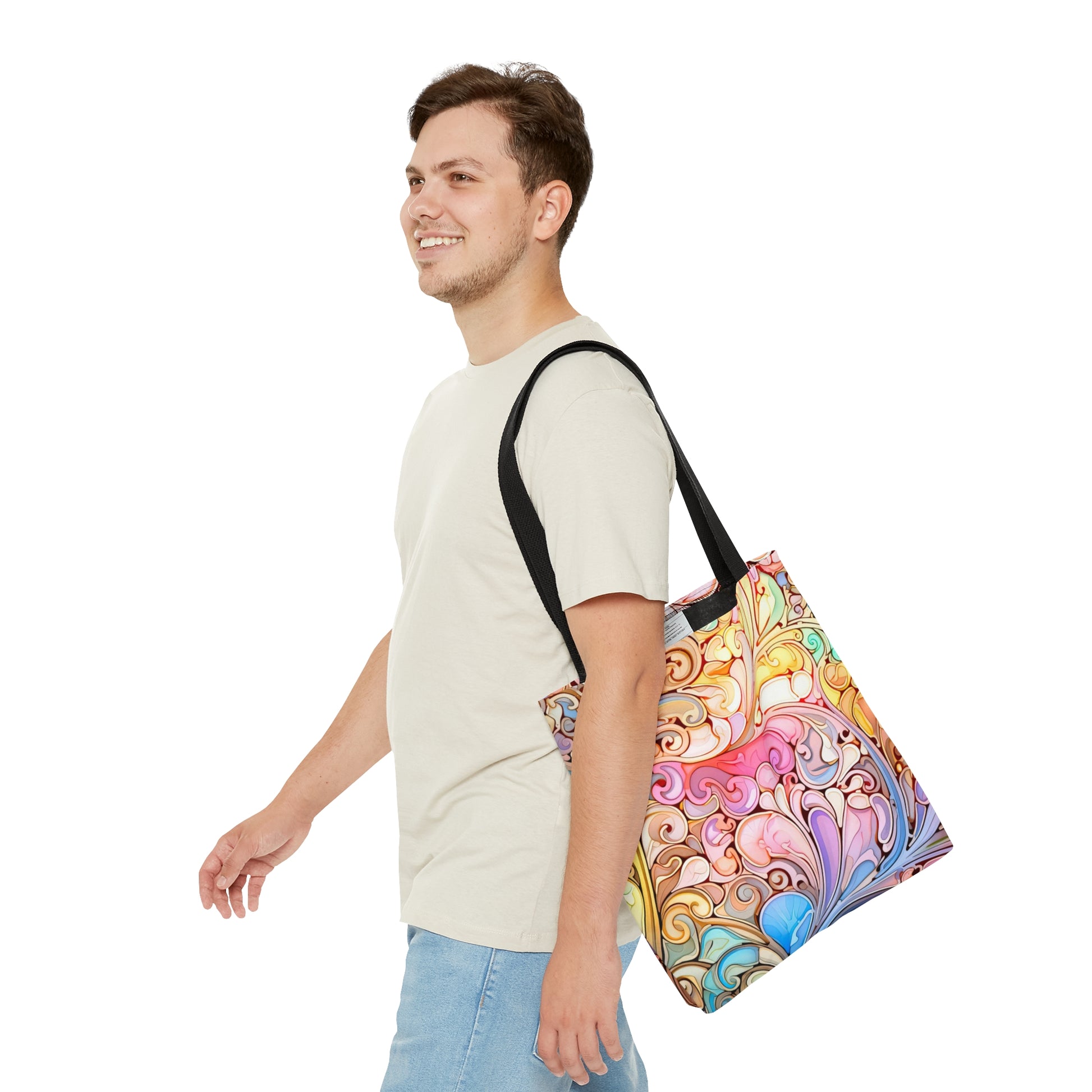 A smiling man in a light beige t-shirt and blue jeans carries a Rainbow Paisley Stained Glass Tote Bag over his shoulder against a white background.