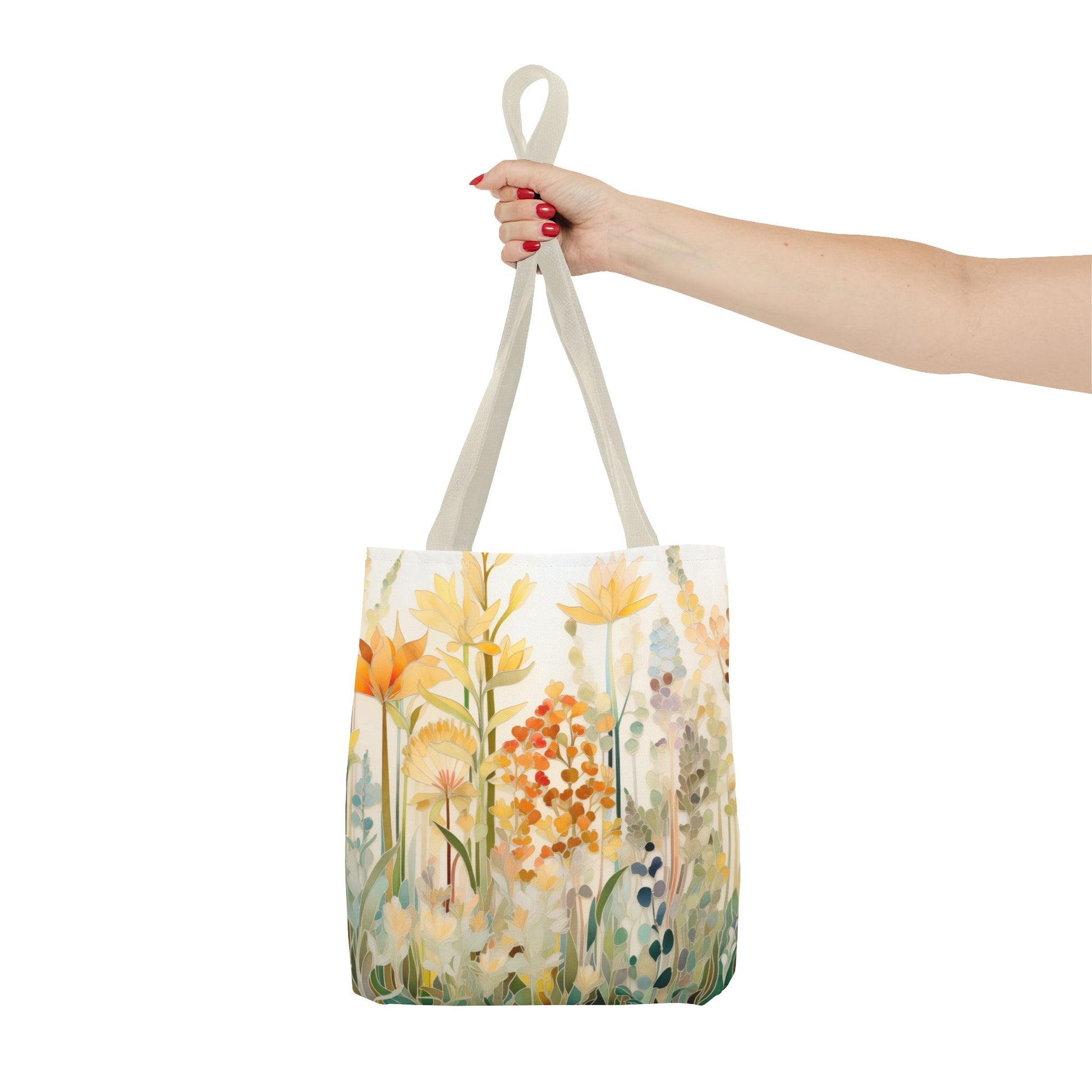 A hand with red nail polish holds the Stained Glass Fall Flowers Tote Bag, showcasing an original artist design of yellow and orange flowers with green foliage on a white background, crafted from durable polyester materials.