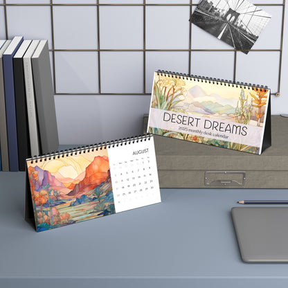 Two desk calendars sit on a desk, one displaying "2025 Desk Calendar - Desert Landscapes" and the other showing August with an illustration of a mountain landscape. Books and a pen are nearby, showcasing the high-quality paper stock and vibrant designs.