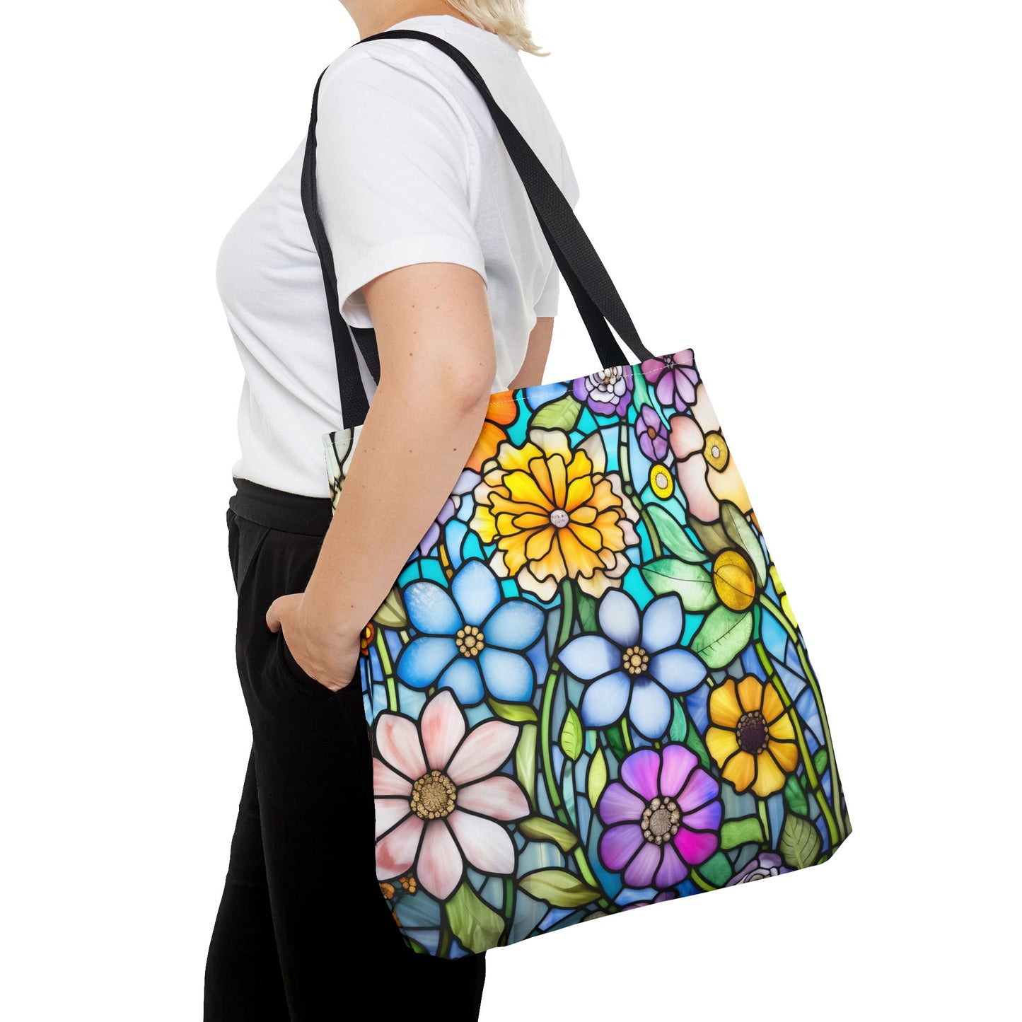 A person in a white shirt and black pants carries the Stained Glass Folk Art Flowers Tote Bag, featuring an original artist design with vibrant blue, pink, yellow, and purple flowers on a plain white background, crafted from durable polyester.