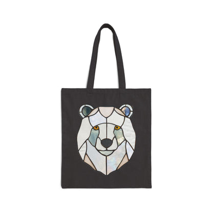 The Stained Glass Polar Bear Cotton Canvas Tote Bag by Noelle Barnes features a geometric polar bear design in shades of white, blue, and gray, with striking orange eyes that contrast beautifully against the pattern.