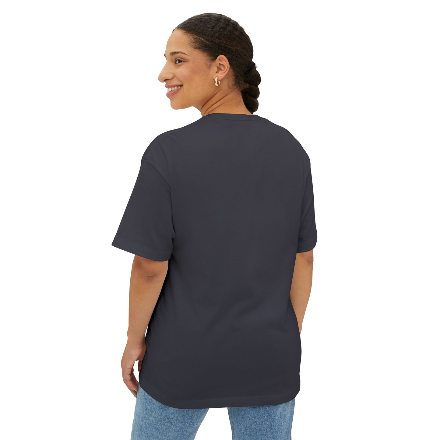 A woman with braided hair, wearing a Stained Glass Hot Air Balloon Oversized Tee Shirt and blue jeans, smiles as she looks over her shoulder against a white background.