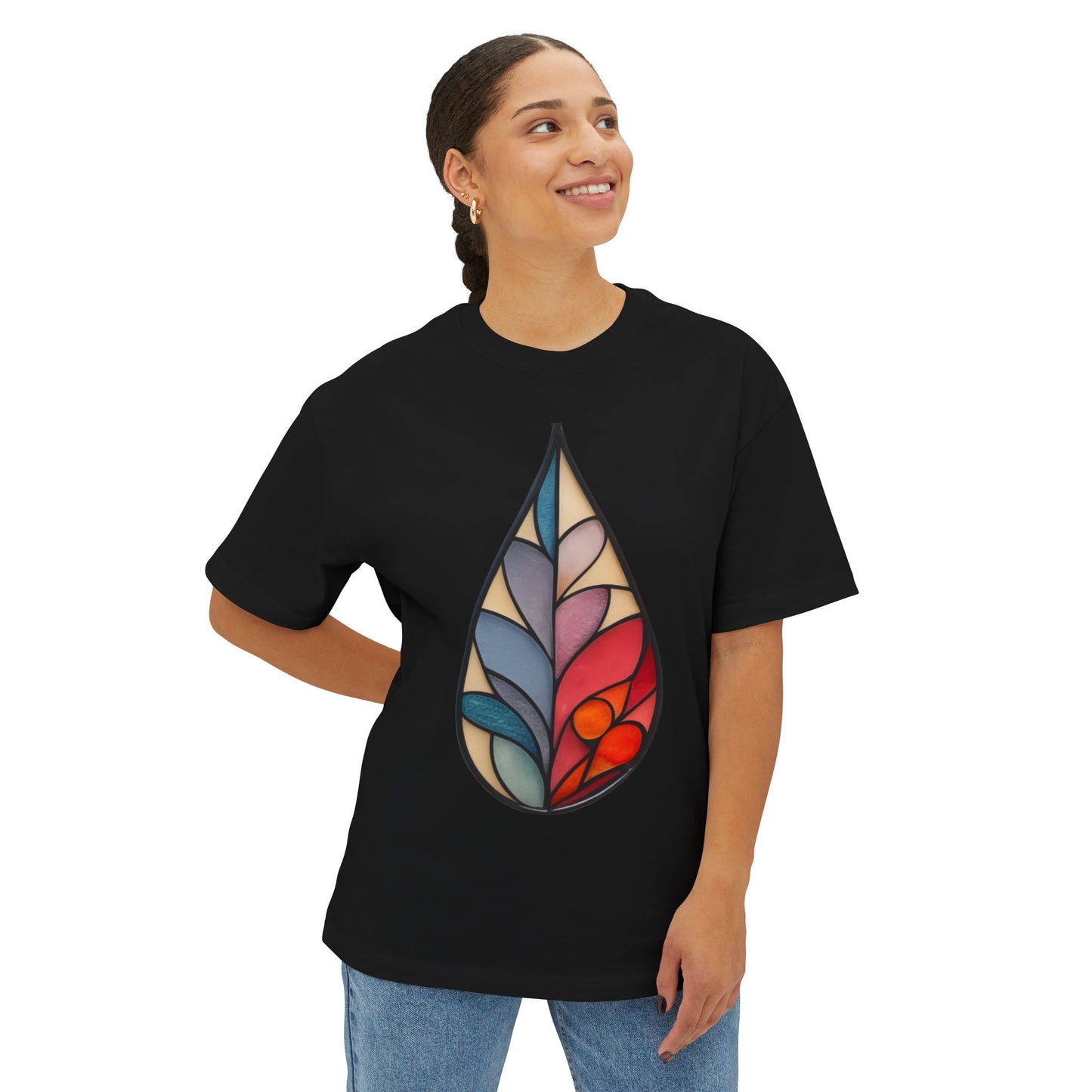 A person stands smiling, wearing a black Stained Glass Botanical Raindrop Oversized Tee Shirt from Bella+Canvas, showcasing a vibrant, abstract teardrop design reminiscent of stained glass.