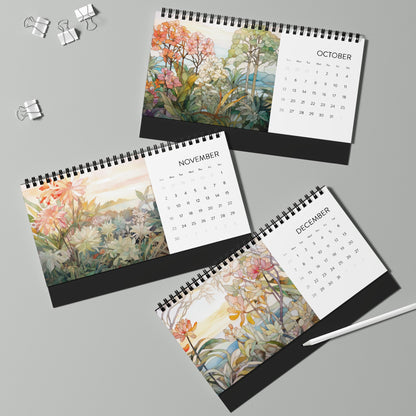 Three open "2025 Desk Calendar - Tropical Flowers" for October, November, and December feature stained glass illustrations of tropical flowers. Two binder clips and a white pen are nearby on a green surface. Made in the USA with meticulous attention to detail, this set adds vibrant artistry to any workspace.