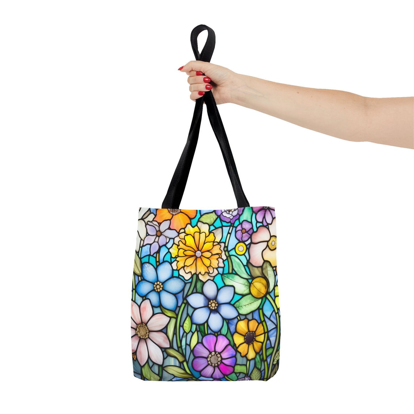 A hand with red nail polish holds the Stained Glass Folk Art Flowers Tote Bag, featuring a colorful floral design and black handles against a white background. Made from durable polyester materials, this piece showcases an original artist's design.