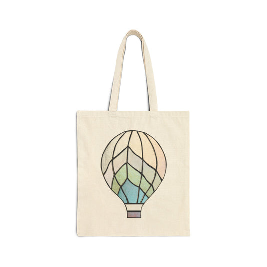 The Stained Glass Hot Air Balloon Cotton Canvas Tote Bag is made of 100% cotton, featuring a vibrant hot air balloon design in blue, green, and beige. It comes with two long handles for easy carrying.