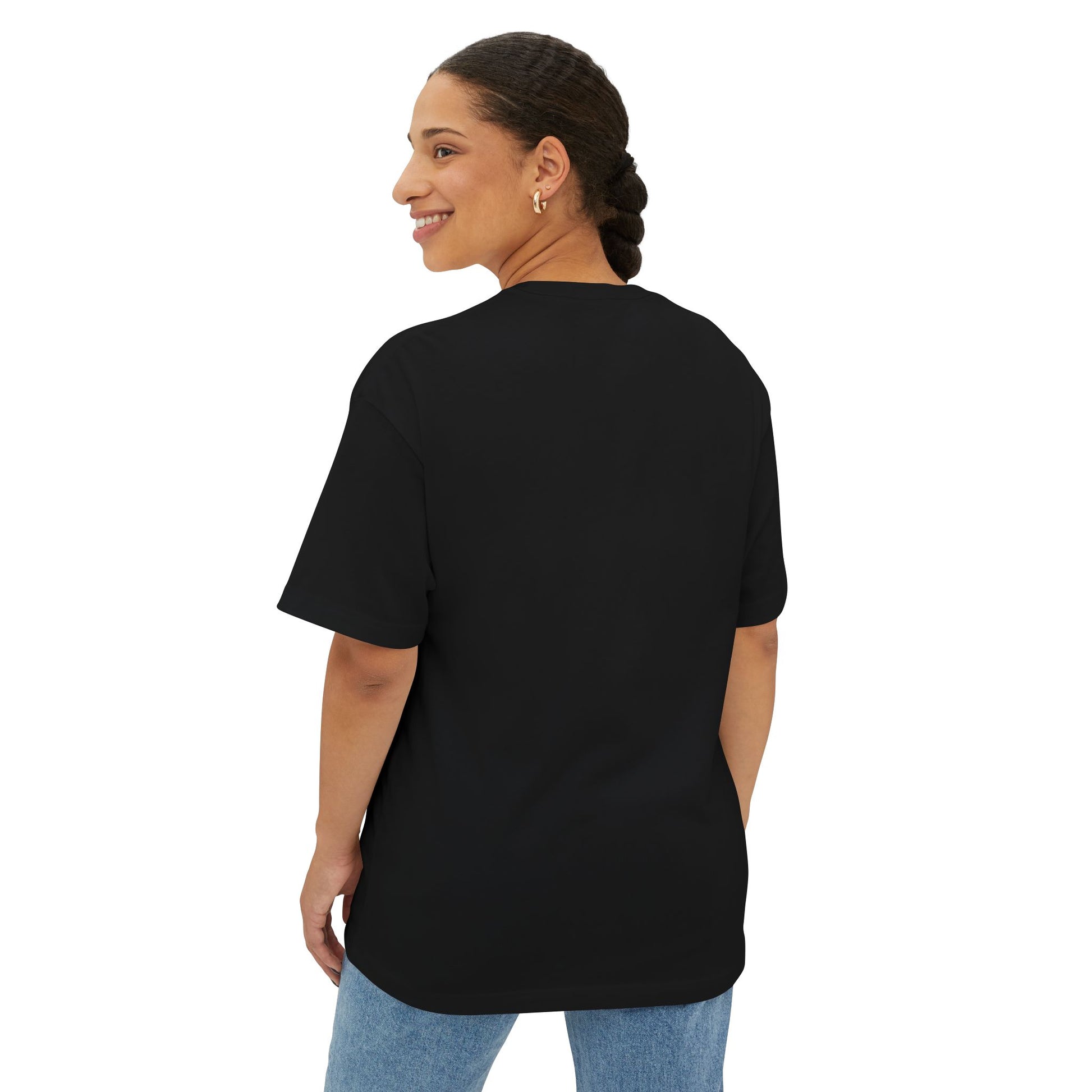 A person with braided hair smiles while wearing a black Stained Glass Botanical Raindrop Oversized Tee Shirt and denim jeans, facing slightly away from the camera.