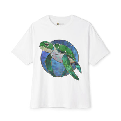 The Stained Glass Turtle Oversized Tee Shirt showcases a stained glass-style illustration of a green sea turtle set against a blue circular background, all on a white Bella+Canvas T-shirt.