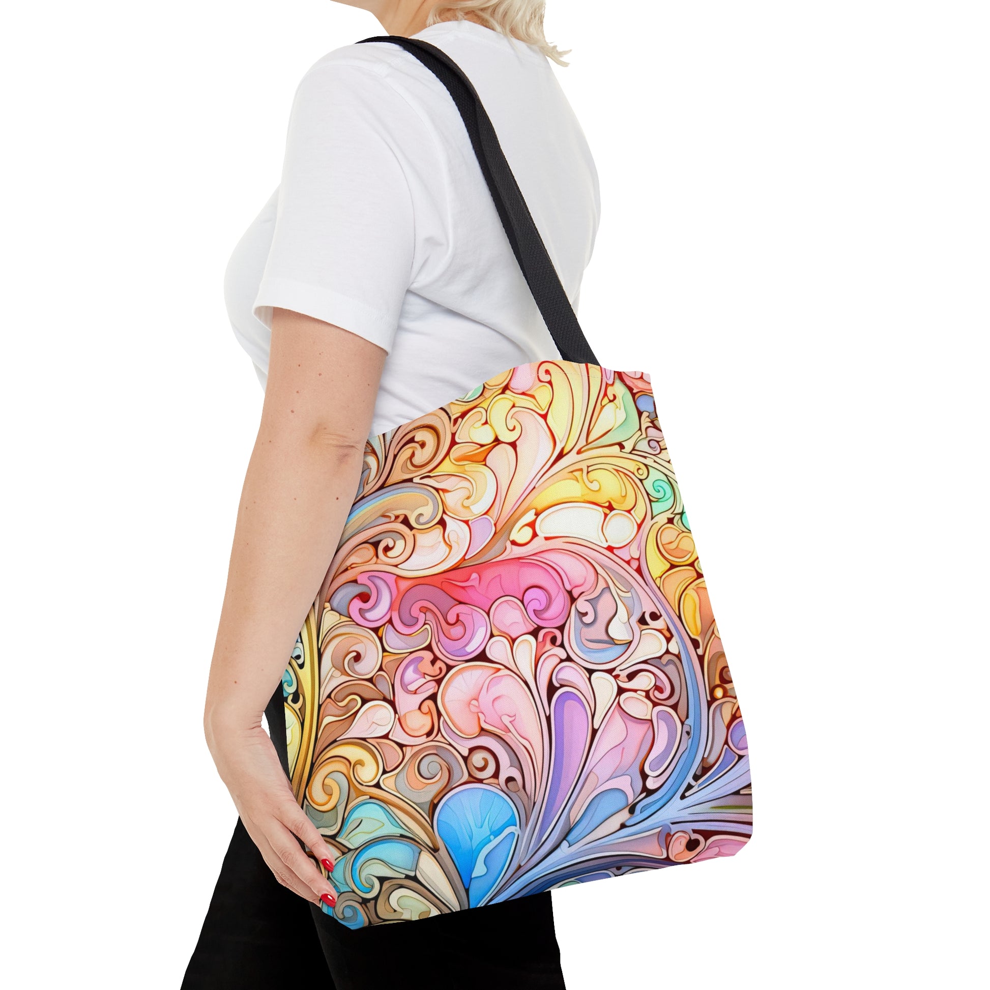 A person holding the Rainbow Paisley Stained Glass Tote Bag, adorned with an intricate, abstract swirling pattern reminiscent of stained glass art, is wearing a plain white shirt and black pants and is shown from the side.