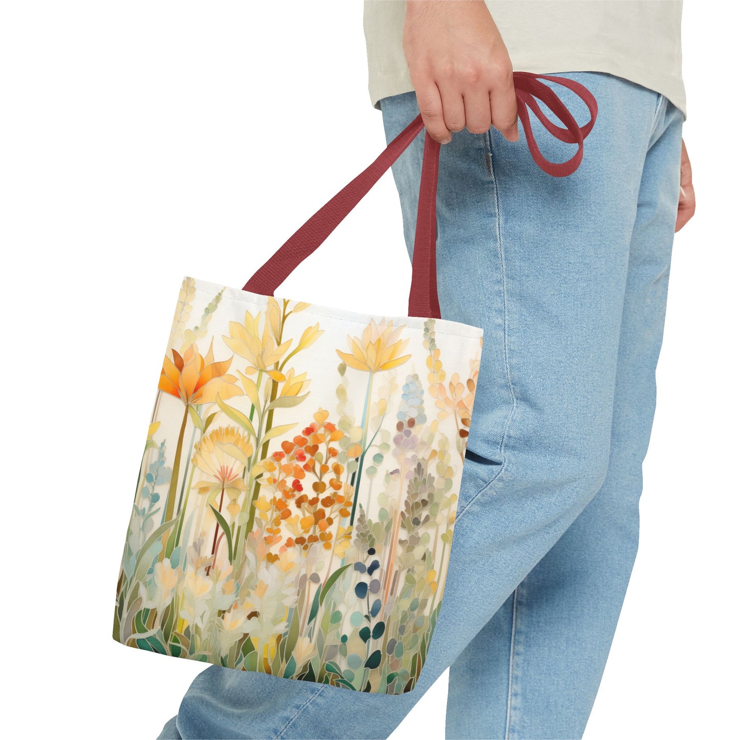 A person holds the Stained Glass Fall Flowers Tote Bag with maroon handles, while wearing light blue jeans and a light-colored shirt. This tote bag, showcasing an original artist design, is made from durable polyester materials.