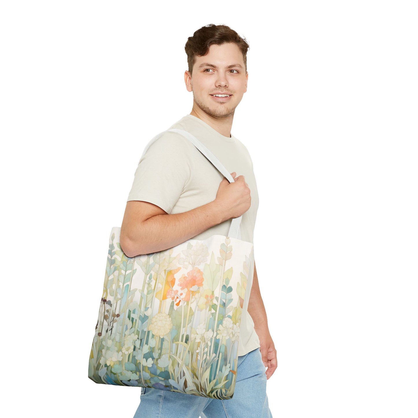 The man, wearing a light gray t-shirt and blue jeans, smiles against a white background. Over his shoulder is the Stained Glass Pastel Flowers Tote Bag, which features an original artist design resembling floral stained glass patterns.