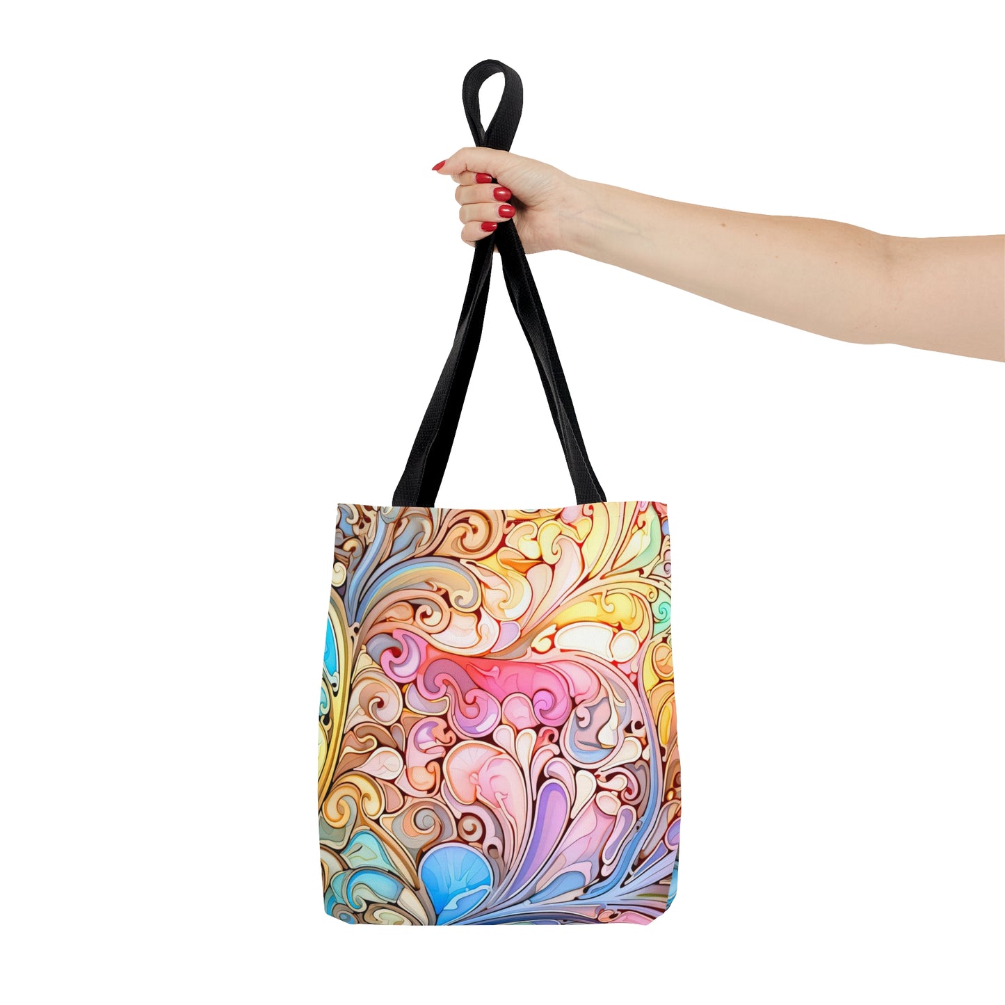 A hand with red nail polish holds the Rainbow Paisley Stained Glass Tote Bag, featuring a vibrant multicolored swirl pattern and black handles—an ideal boho gift available in three sizes.